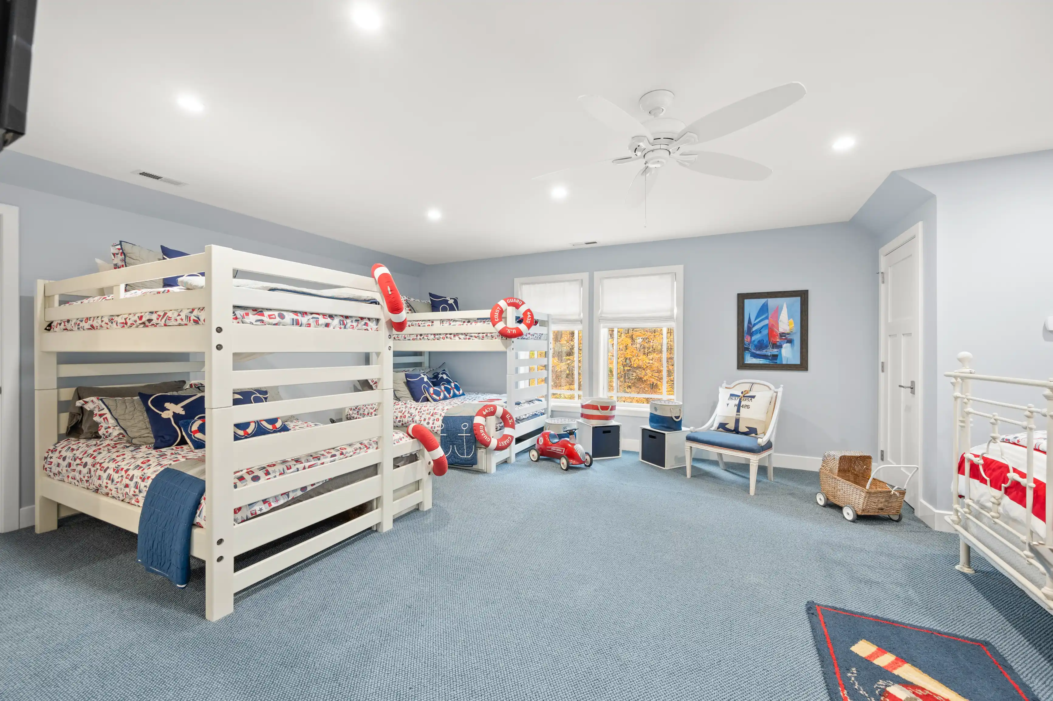 Spacious children's room with nautical theme, featuring a bunk bed with sailboat bedding, lifebuoy decorations, toy chest, and a wall with framed sailboat art.