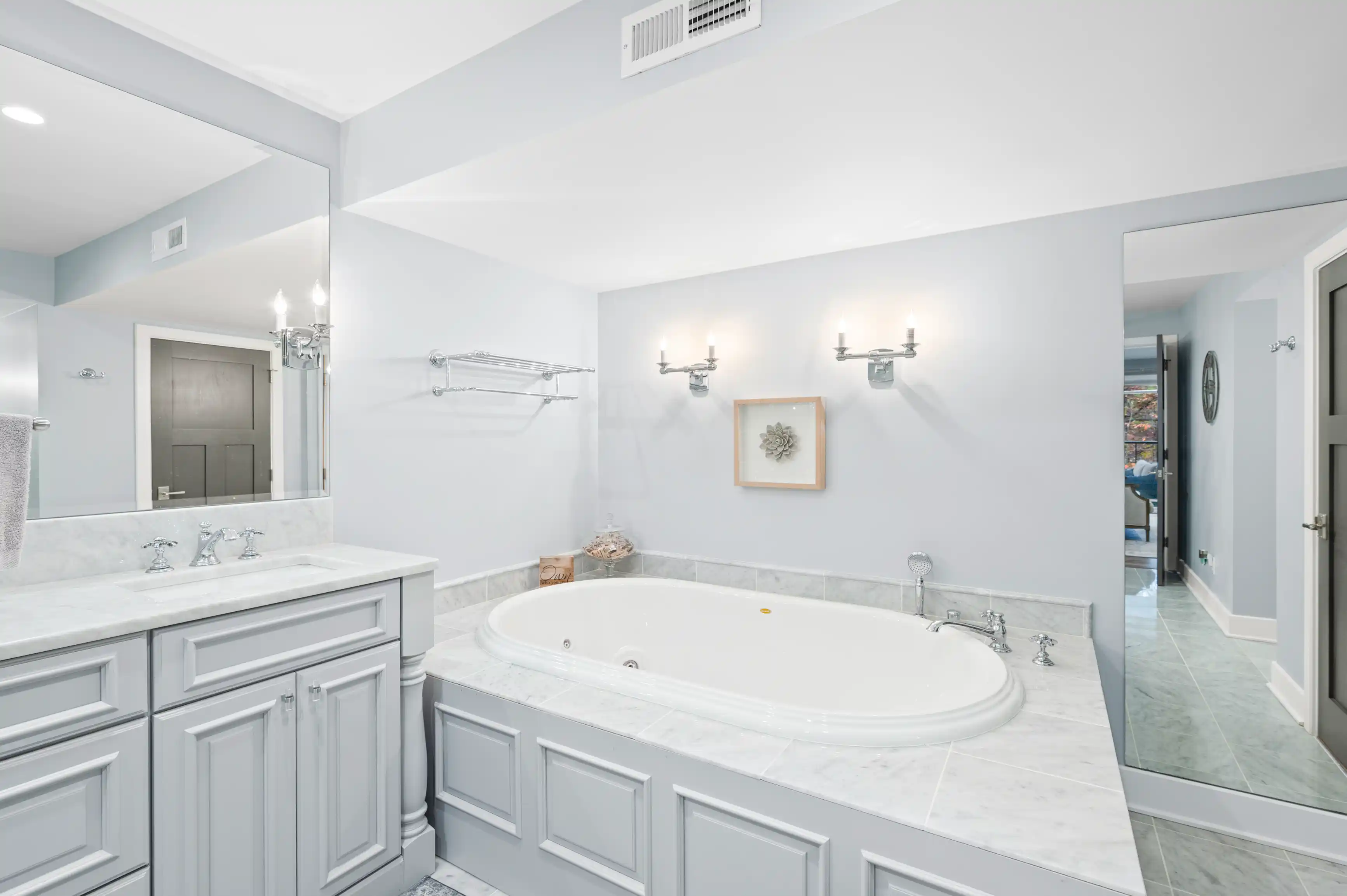 Spacious modern bathroom with large mirror, dual sink vanity, marble countertops, and built-in bathtub.