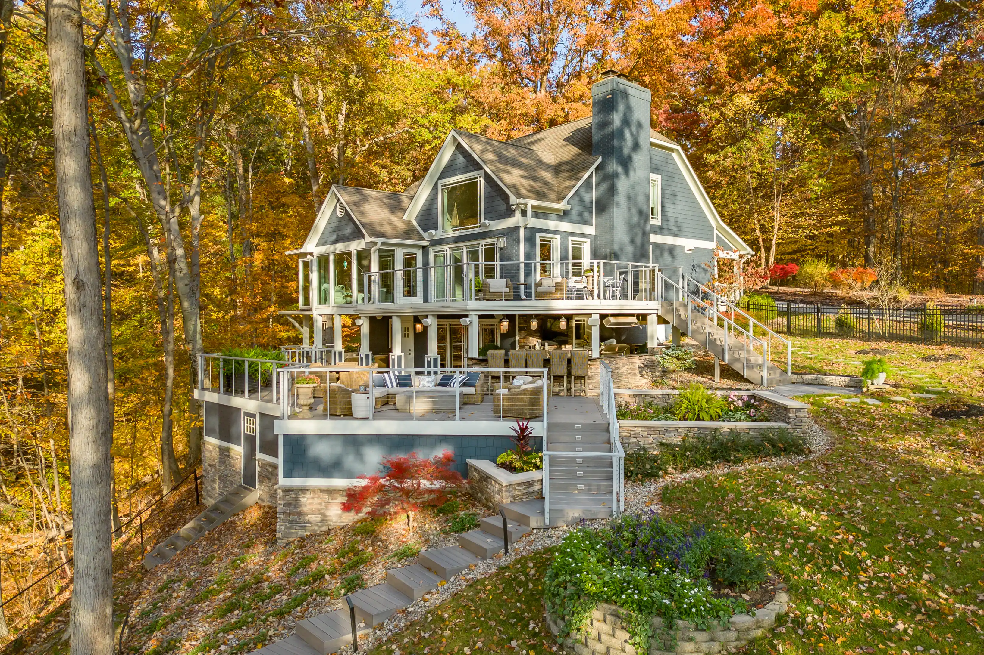 A large two-story house with multiple decks surrounded by autumn trees.
