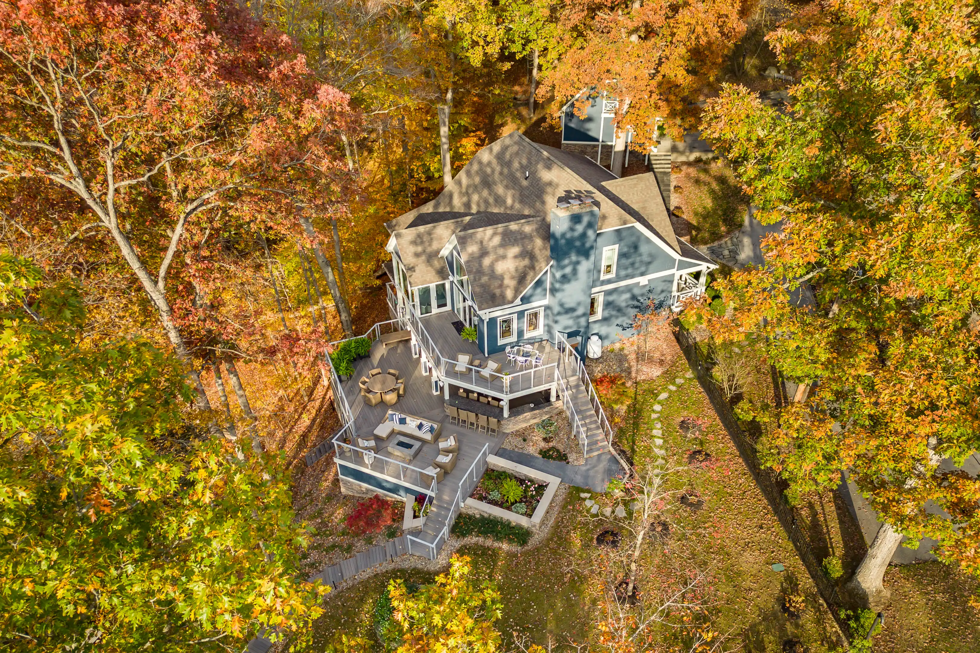 Aerial view of a two-story house with a gray roof and multiple decks surrounded by trees with autumn foliage.