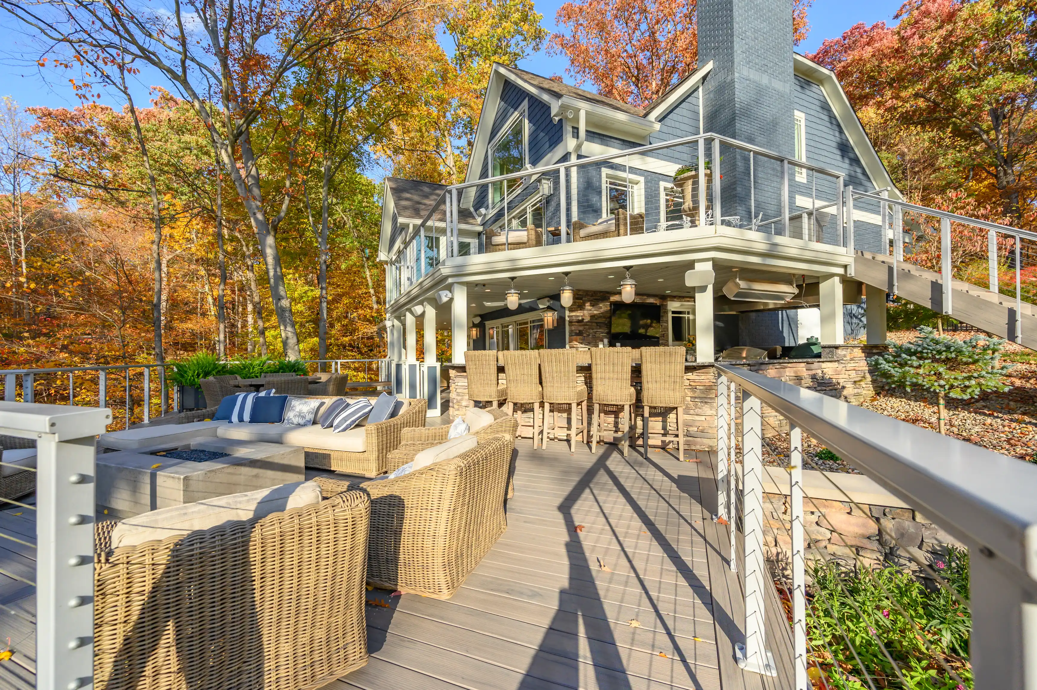 Spacious deck area with outdoor furniture in front of a two-story house with autumn-colored trees in the background.
