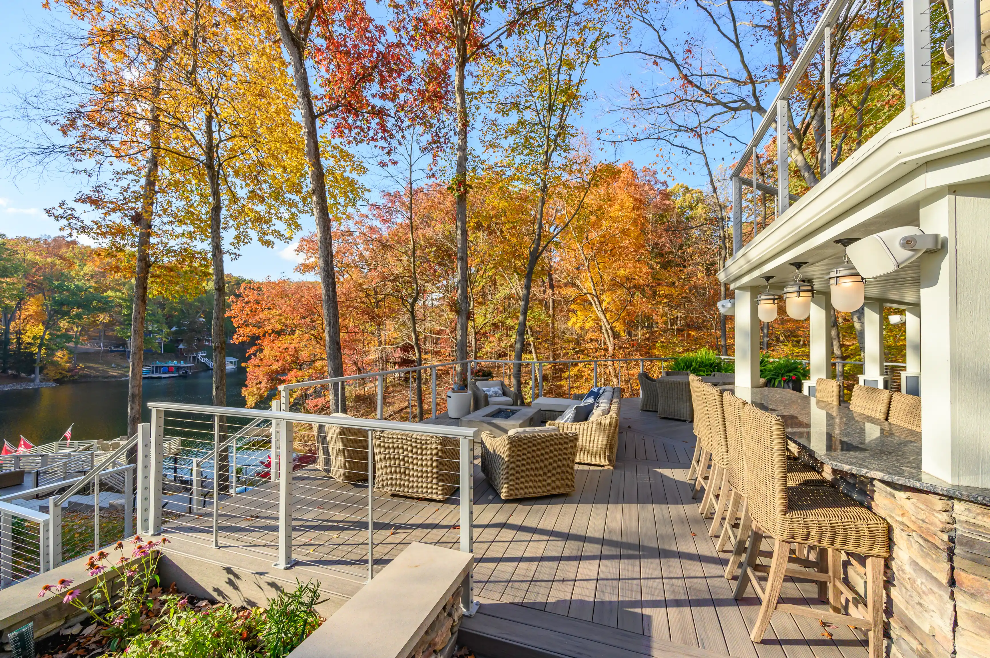 Spacious outdoor deck with wicker furniture overlooking a lake surrounded by autumn-colored trees.