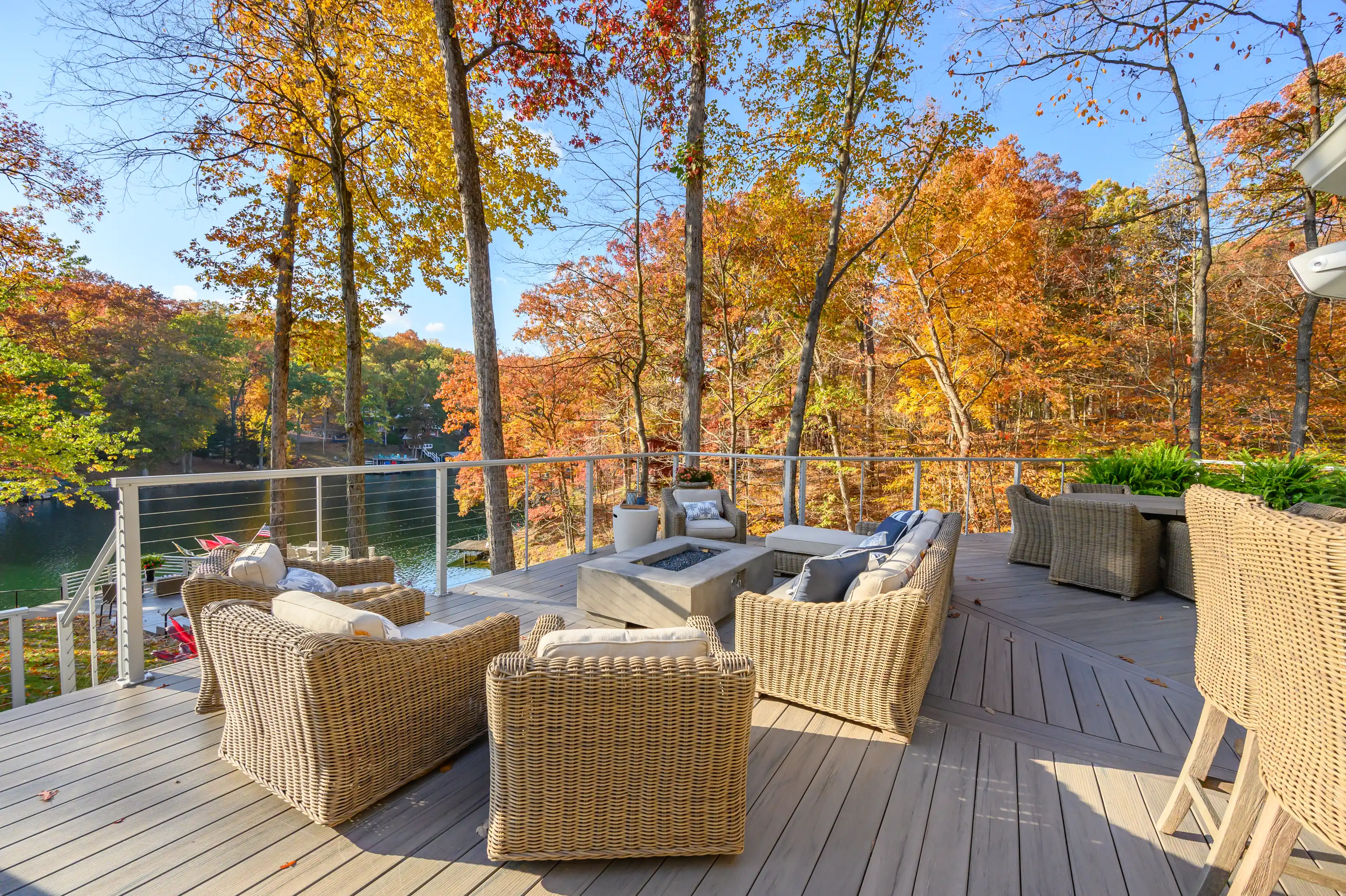Alt text: "Spacious outdoor deck with wicker furniture overlooking a tranquil lake surrounded by colorful autumn trees."