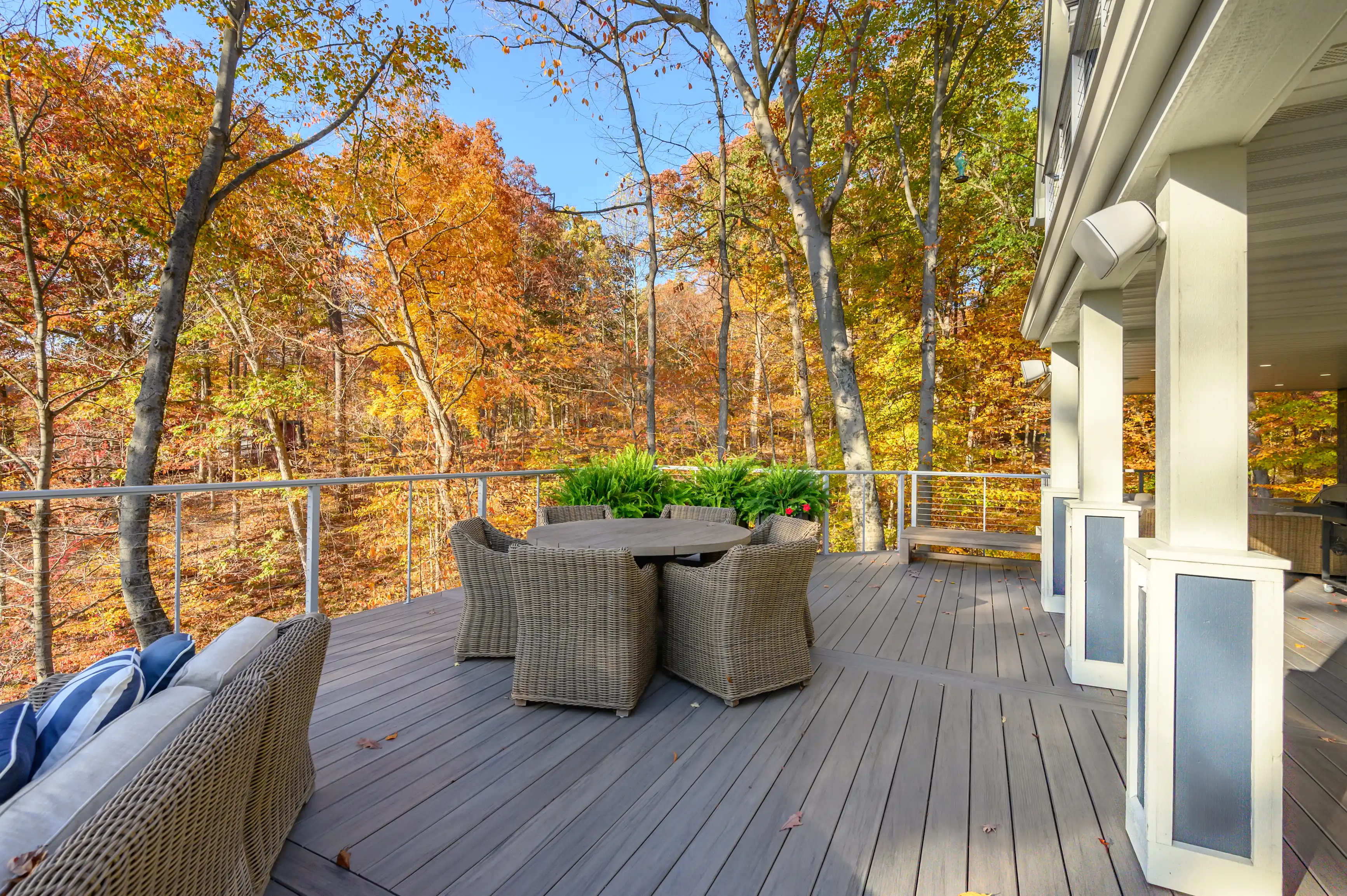 A spacious wooden deck with outdoor furniture overlooking a forest with autumn-colored leaves.