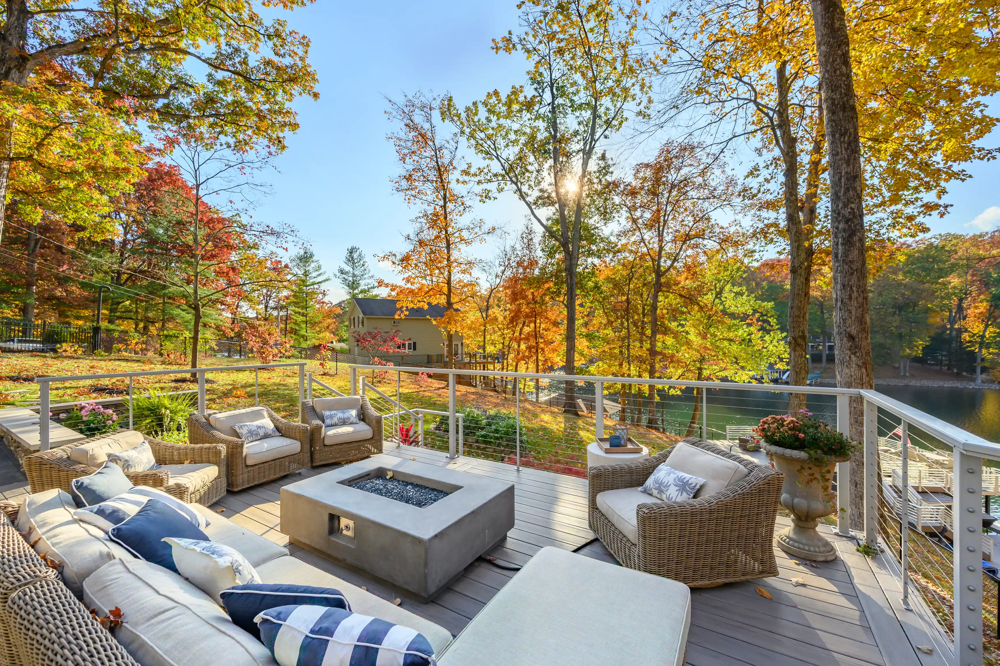 A cozy outdoor patio with wicker furniture overlooking a serene lake surrounded by trees with autumn foliage.