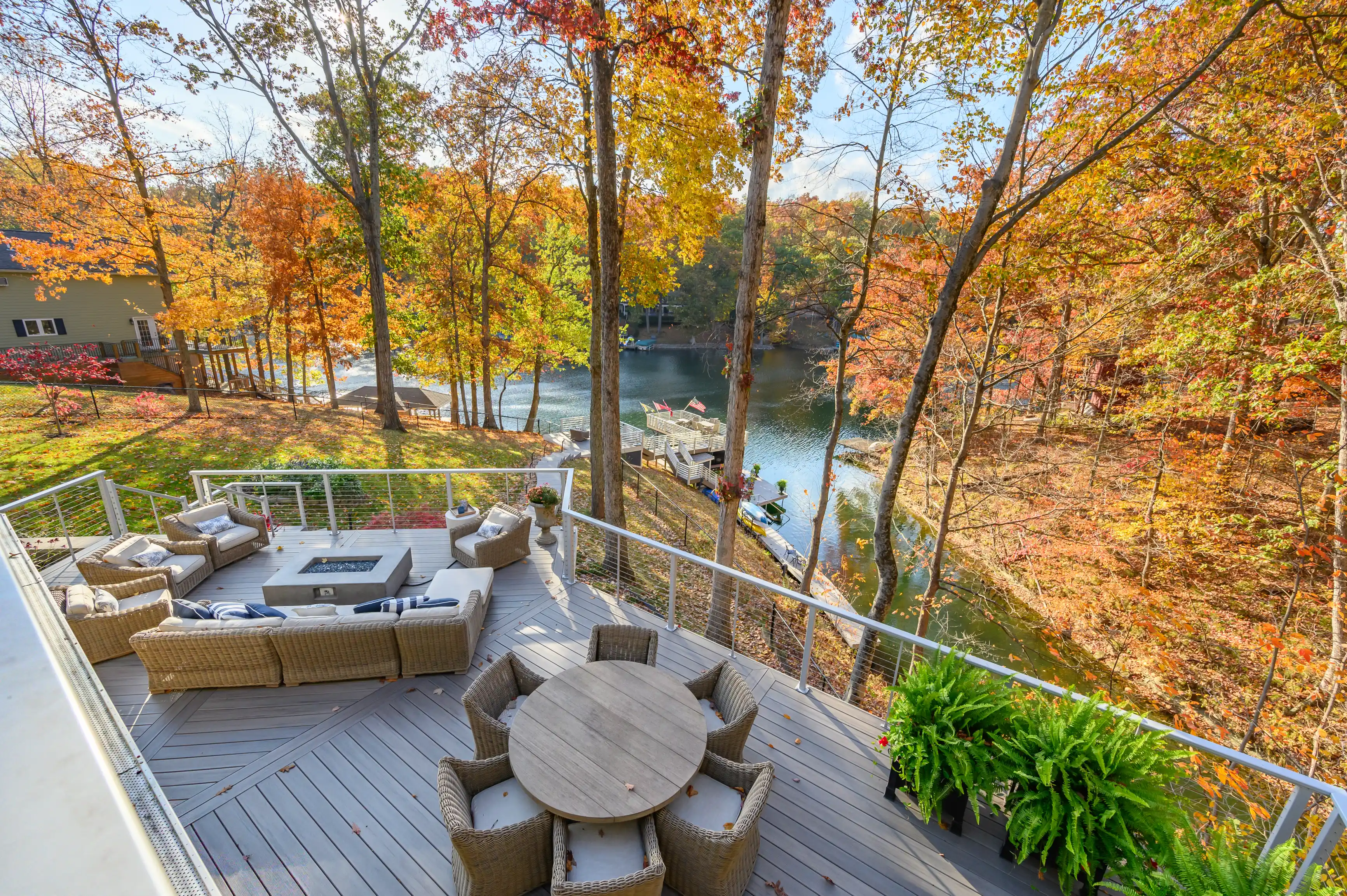 Elevated wooden deck with outdoor furniture overlooking a tranquil lake surrounded by autumn-colored trees.