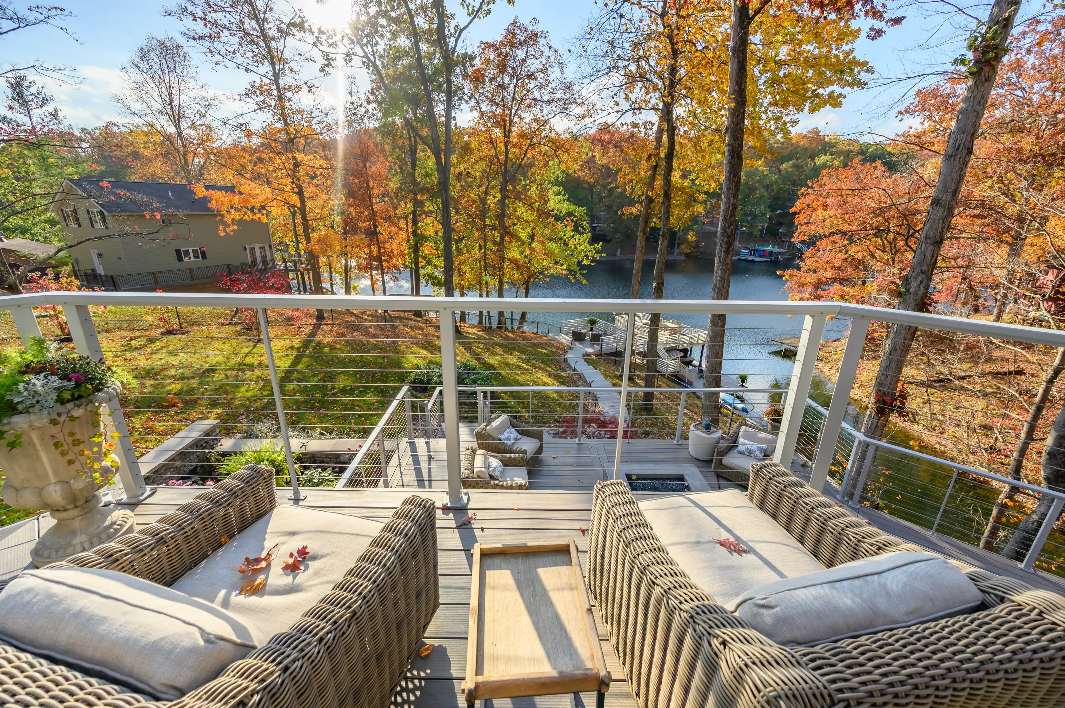 View from a balcony with outdoor furniture overlooking a beautiful autumnal lakeside scene with colorful trees and a clear sky.