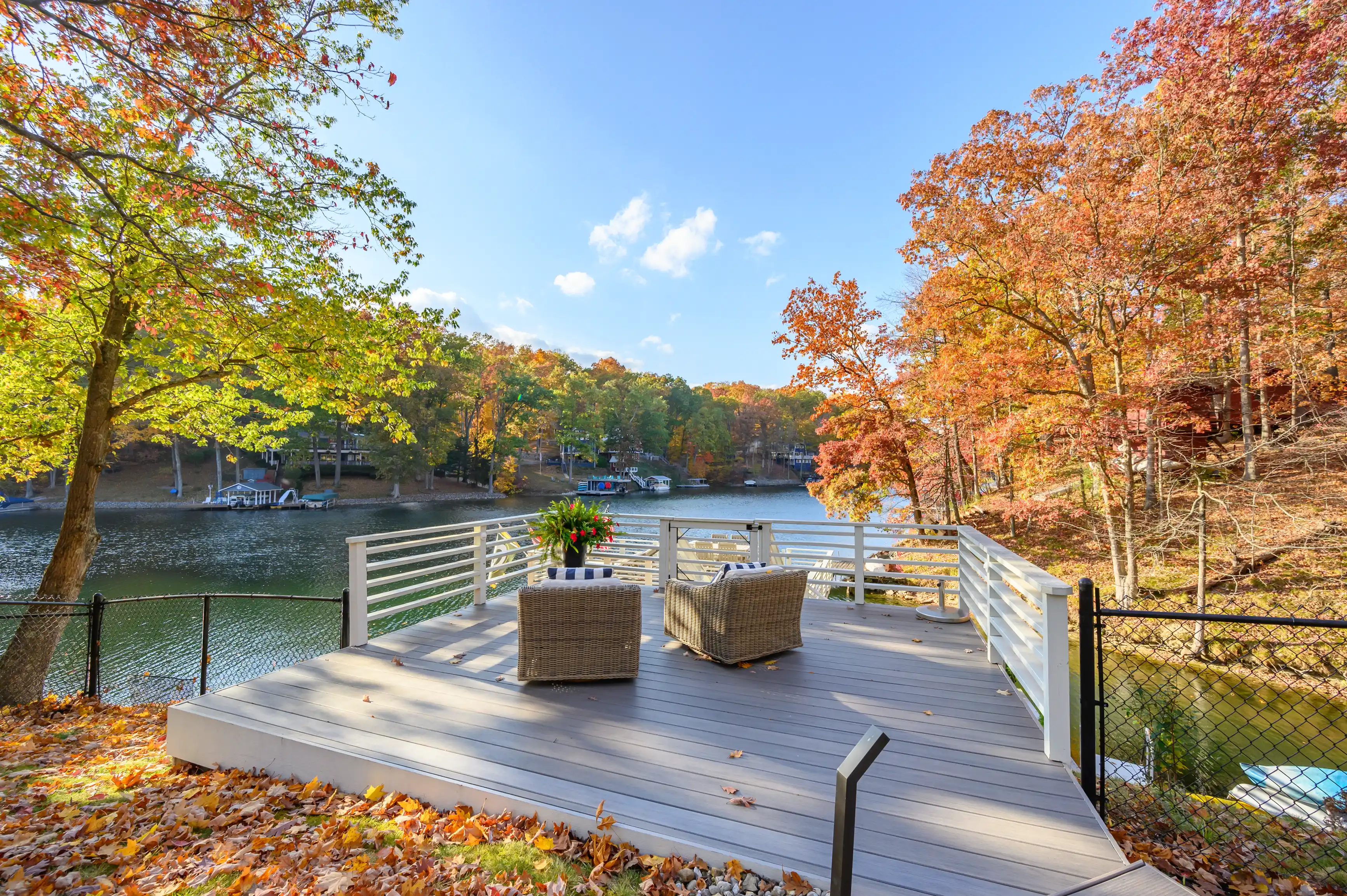 Autumnal view from a lakeside deck with colorful foliage, outdoor furniture, and boats on the water.