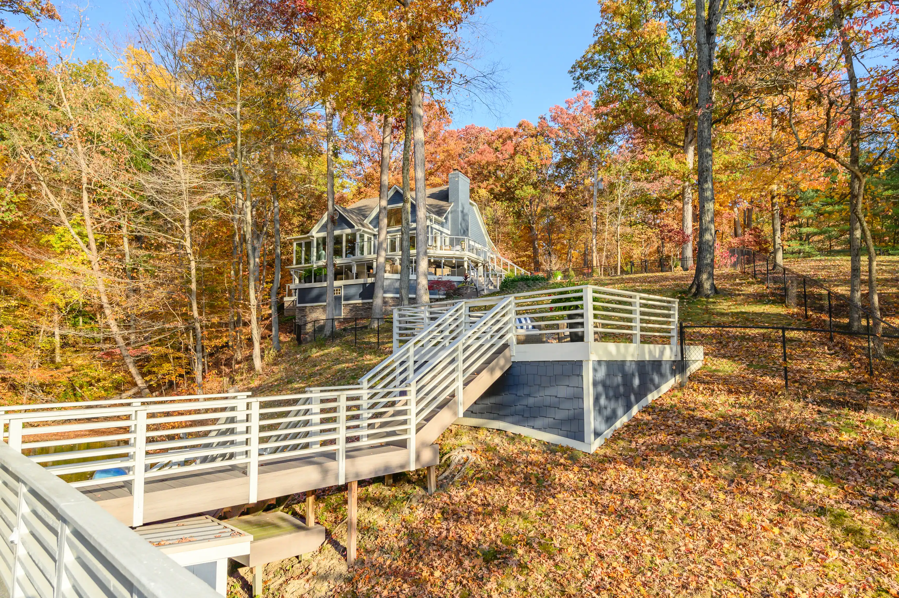 A wooden ramp leading to a large house surrounded by autumn trees with colorful foliage.