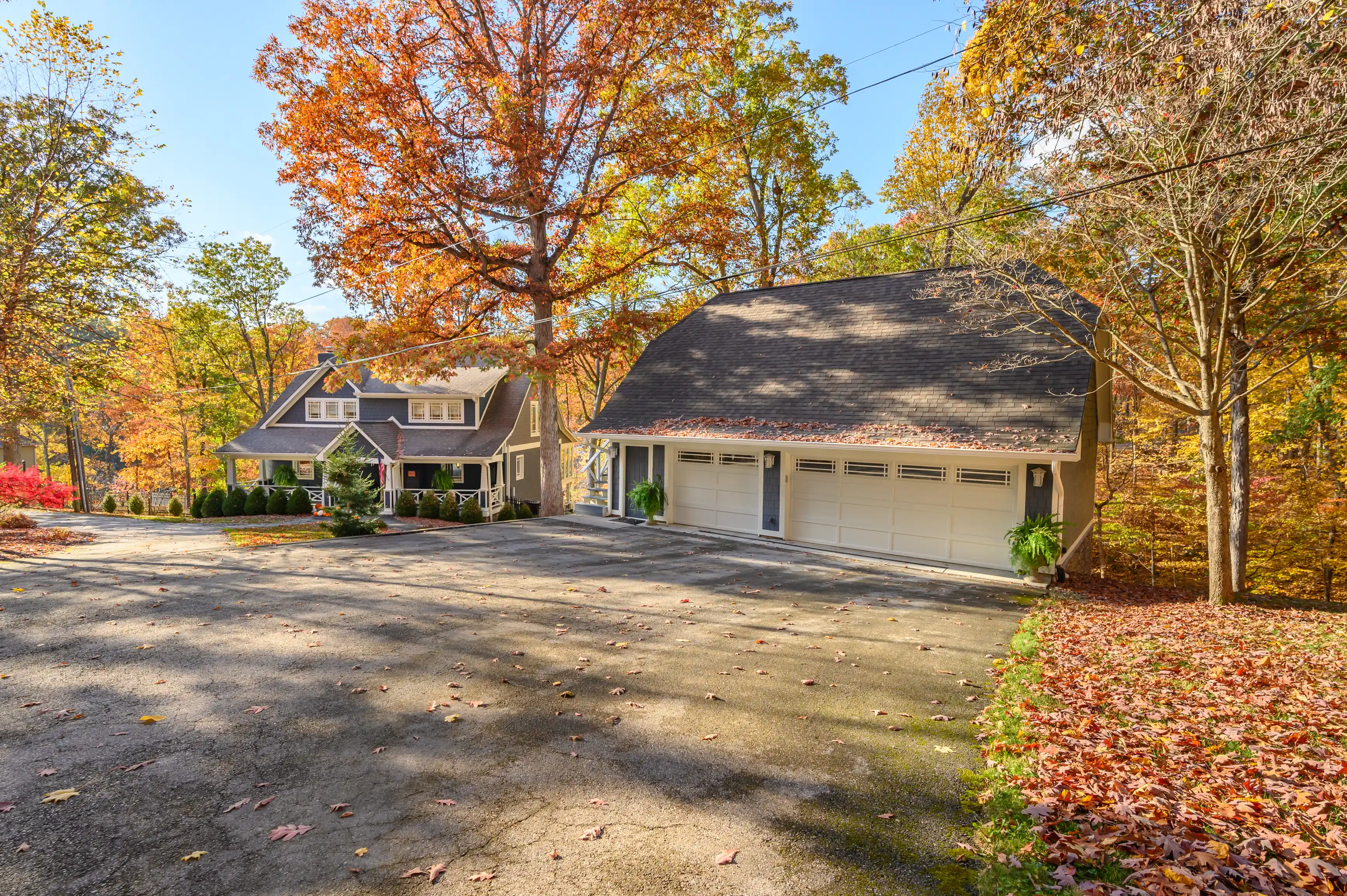 Residential suburban home with a detached three-car garage surrounded by autumn foliage.
