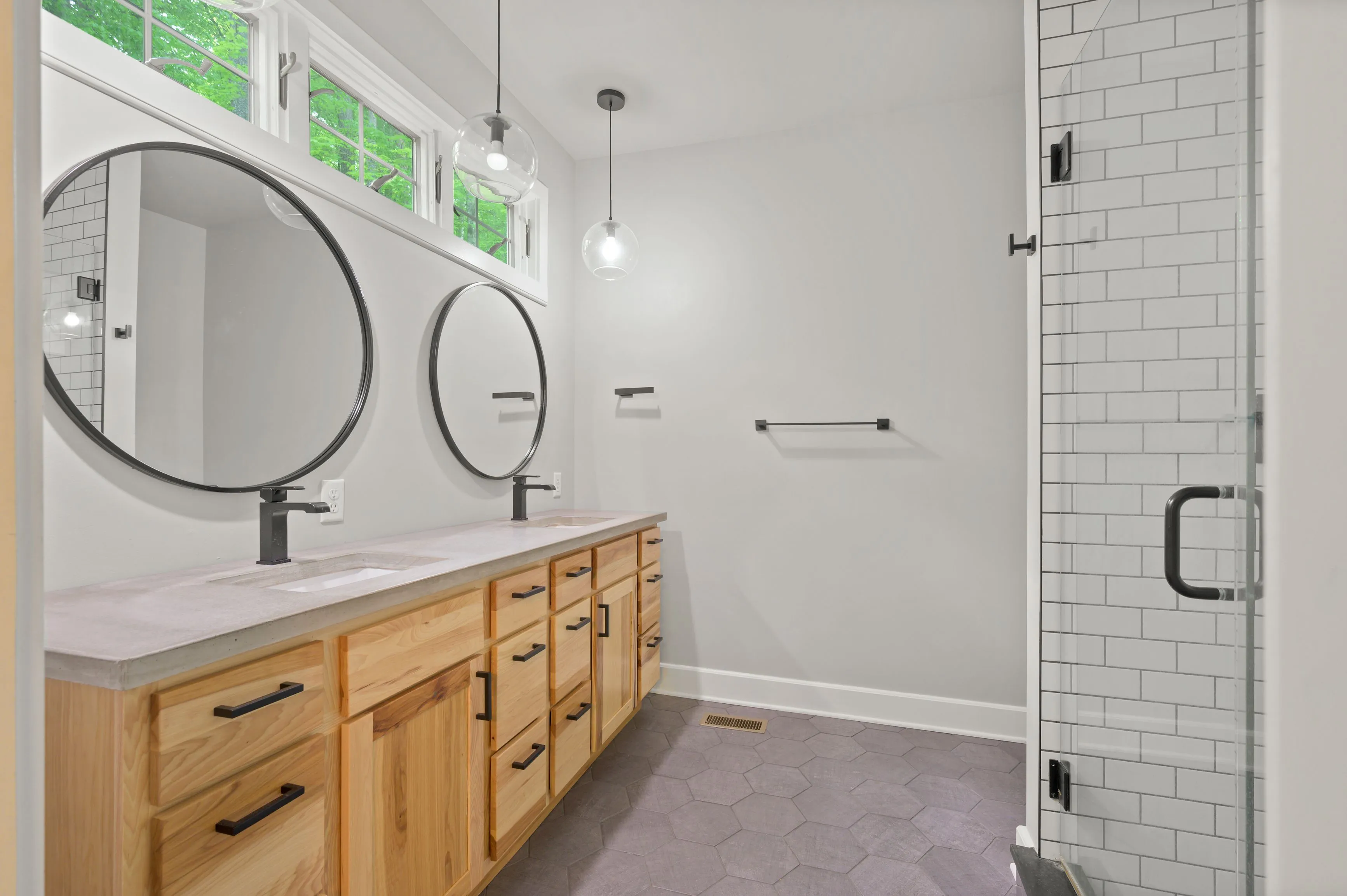 Modern bathroom interior with wooden vanity cabinet, double round mirrors, glass shower and subway tiles.