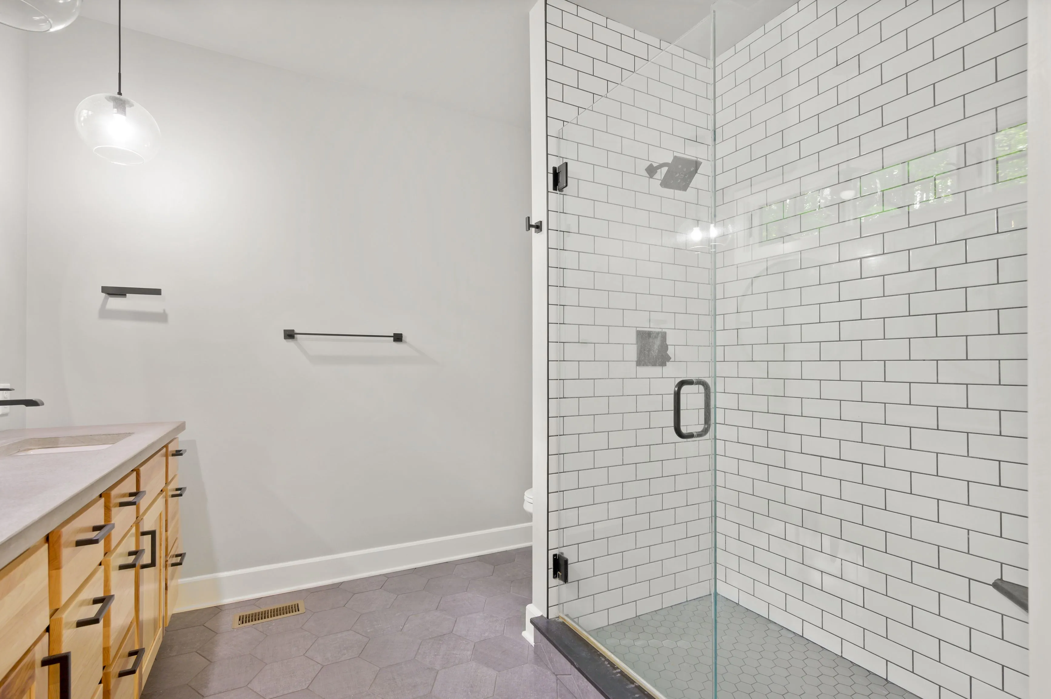 Modern bathroom interior with glass-enclosed shower, white subway tiles, and wooden vanity.