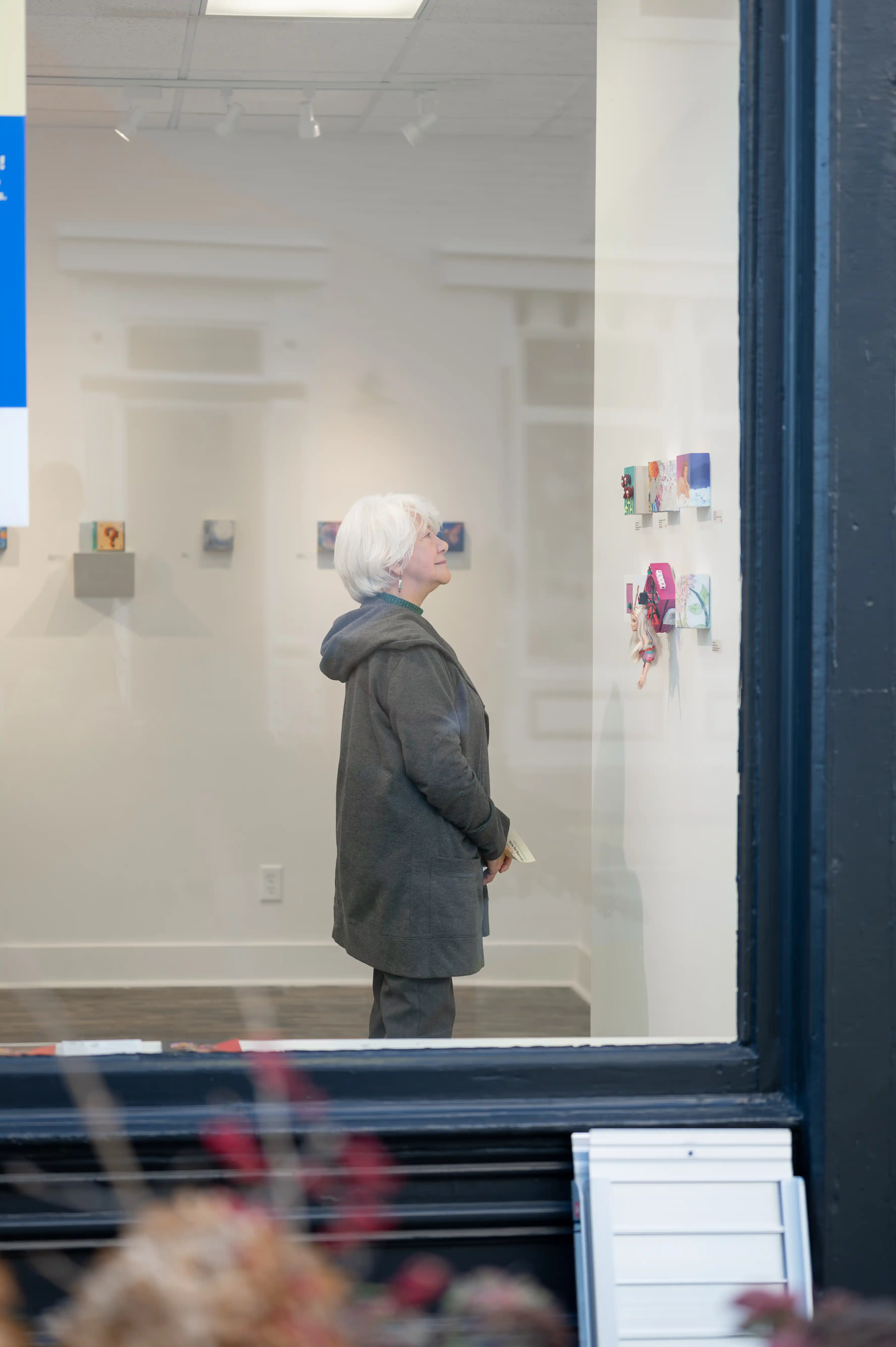 Person standing and looking at artwork in a gallery through the display window.