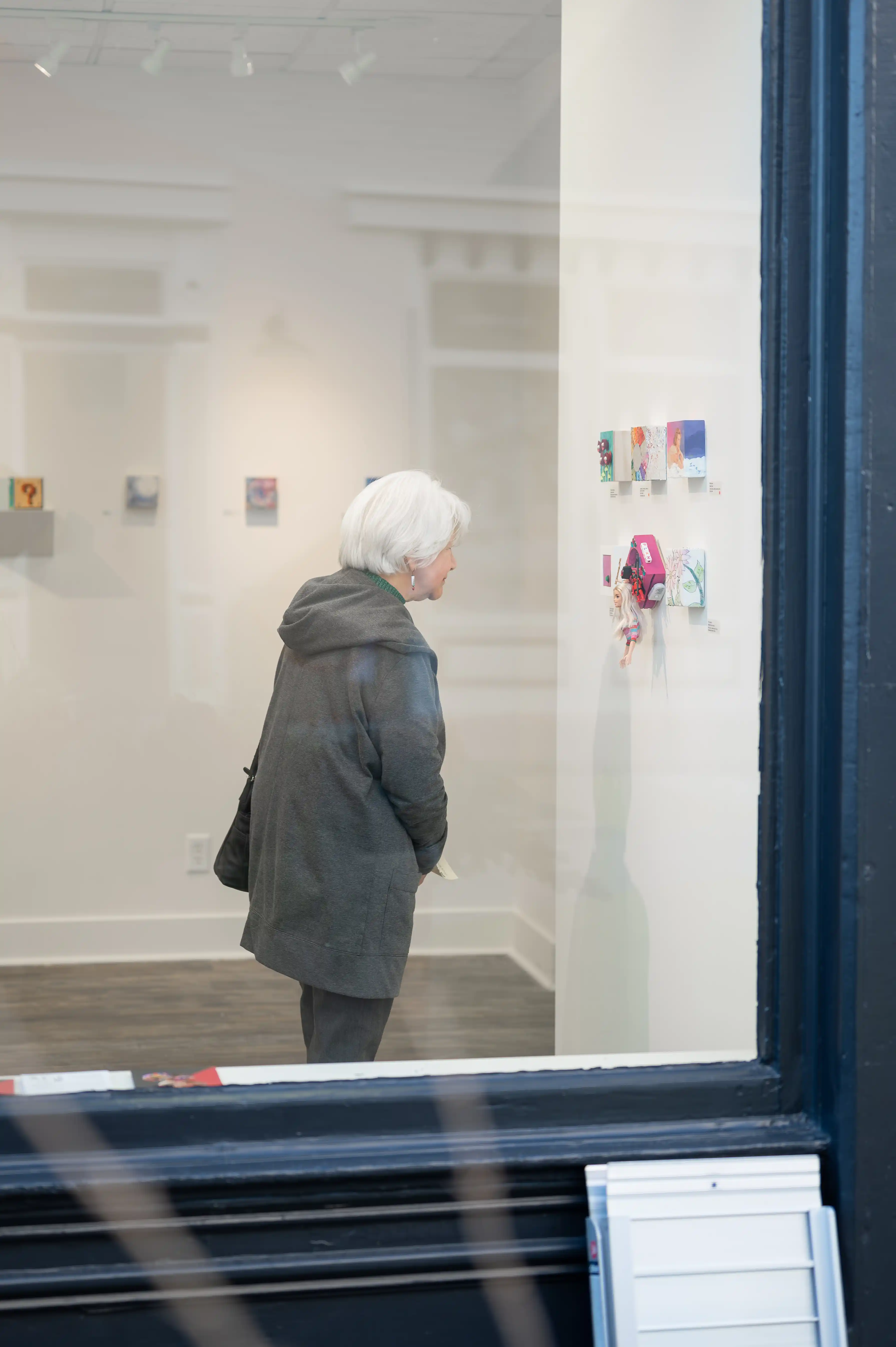 Person viewed through a window, looking at artwork in a gallery setting.