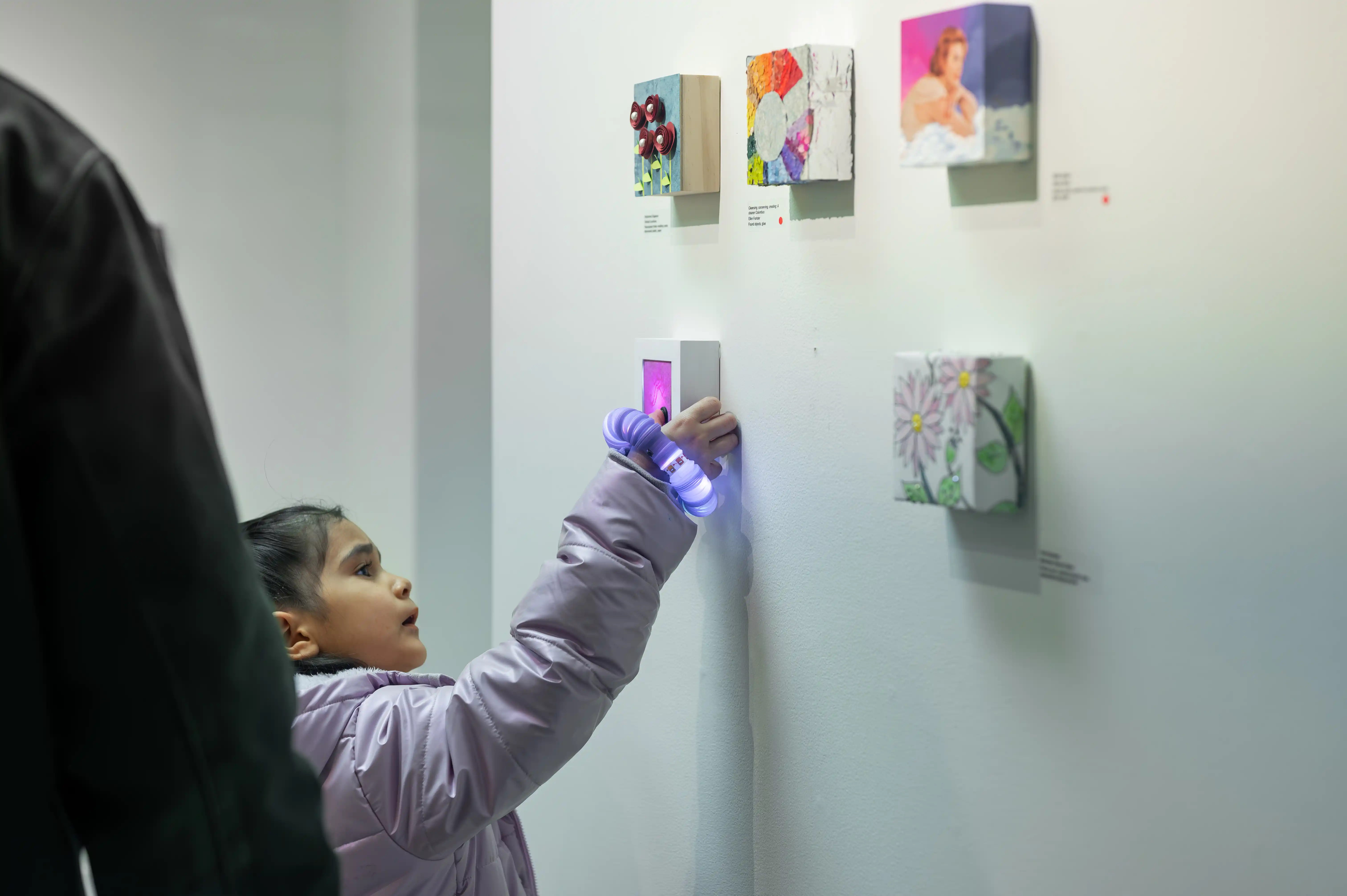 Child in a museum interactively lighting up miniature artworks with a handheld ultraviolet lamp.