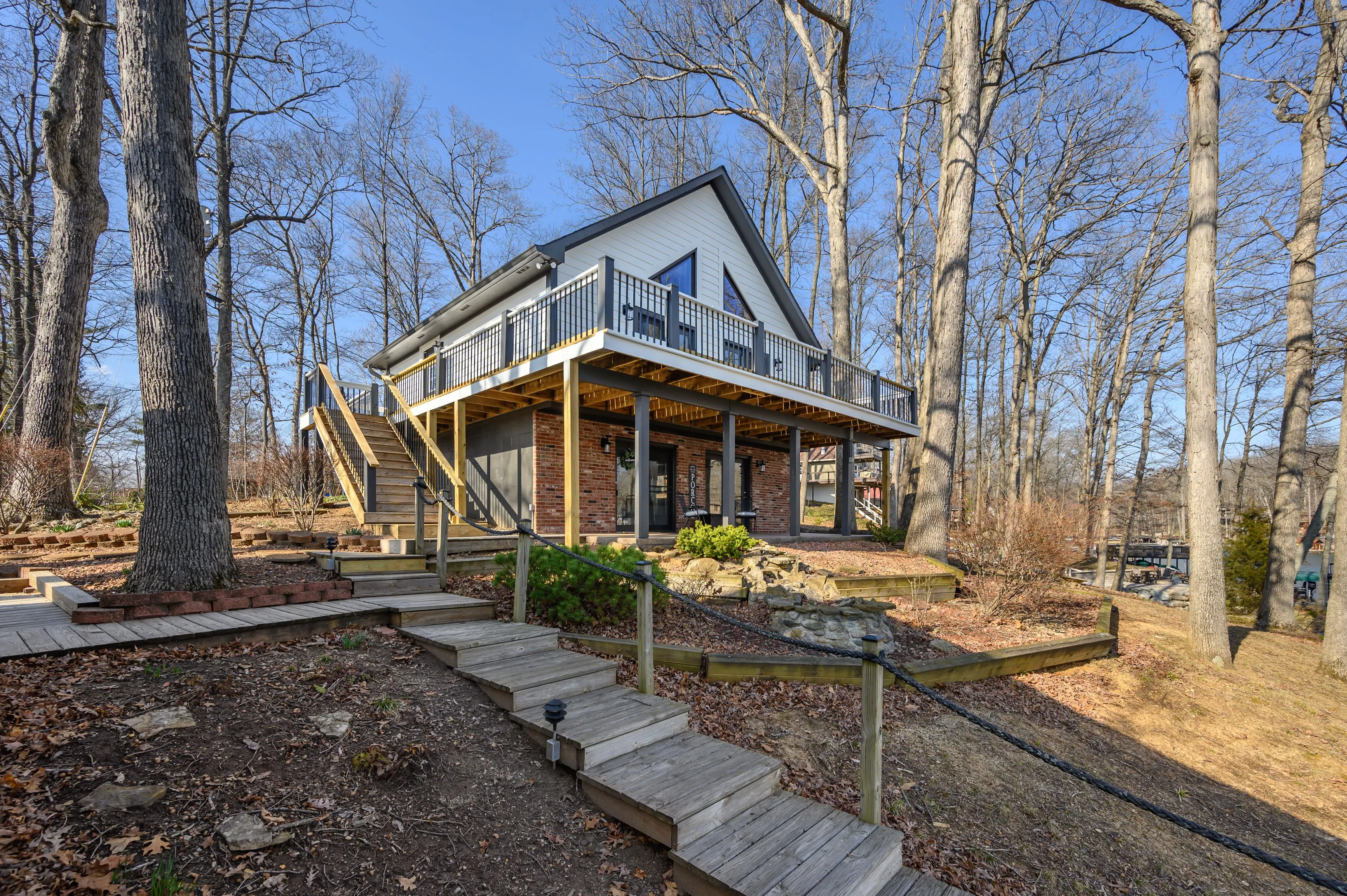  A cozy two-story house nestled among bare trees with a staircase leading to the front porch, showcasing clear blue skies in the background.