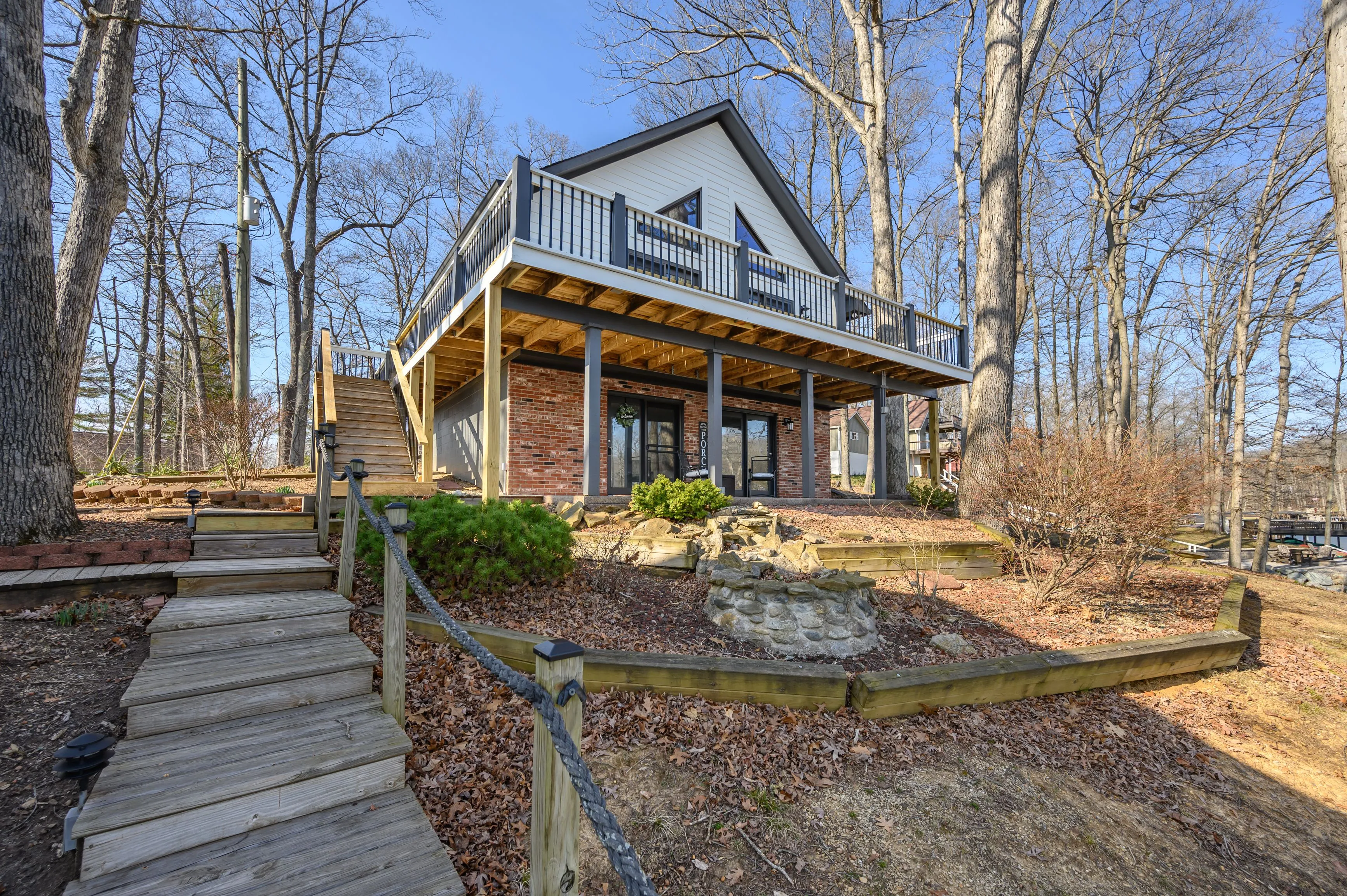 Charming two-story house with a large front porch surrounded by bare trees under a clear sky.