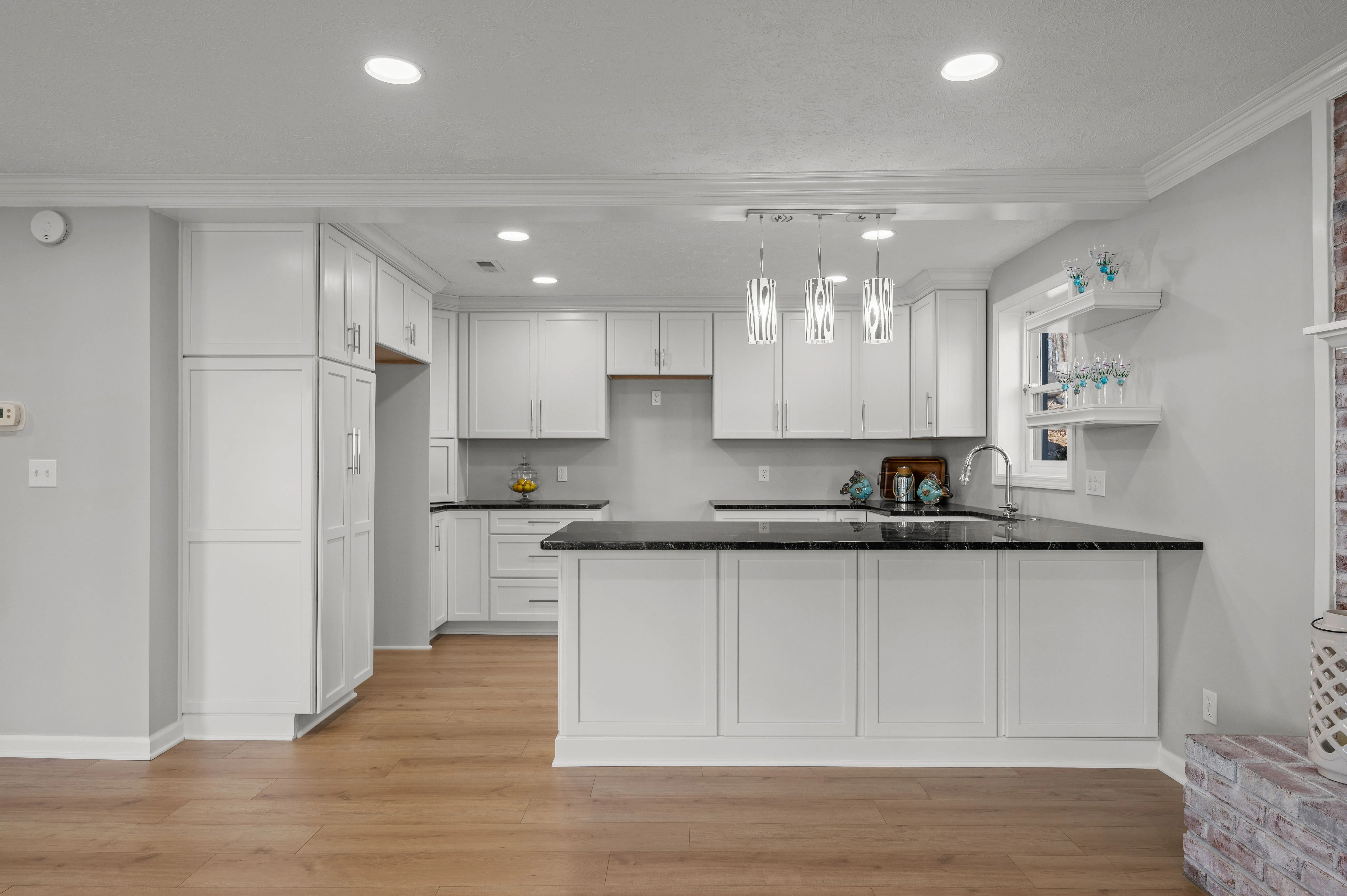 Modern kitchen interior with white cabinetry, black countertops, and hardwood floors.