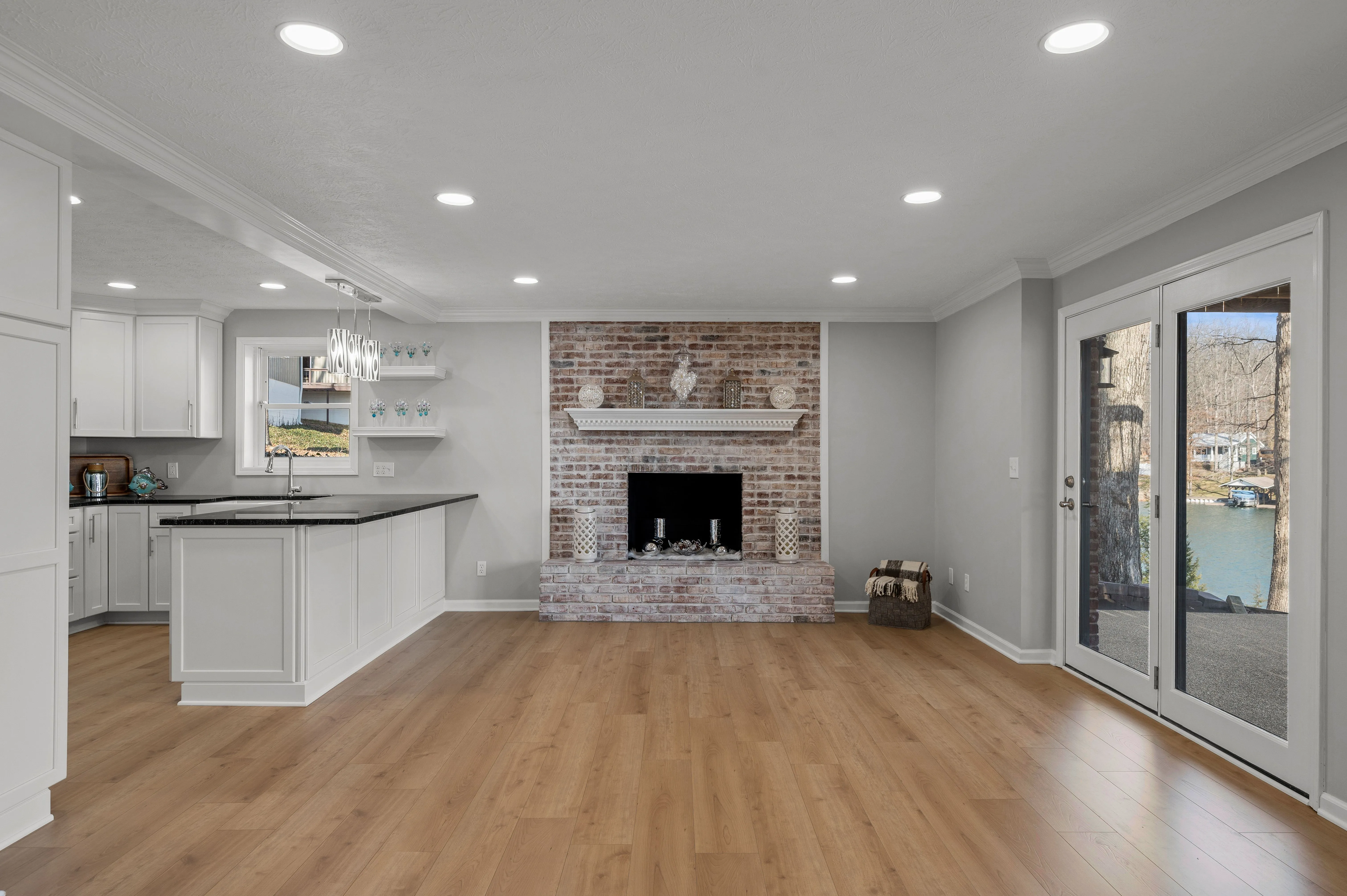 Modern open concept living space with kitchen, hardwood floors, and brick fireplace.