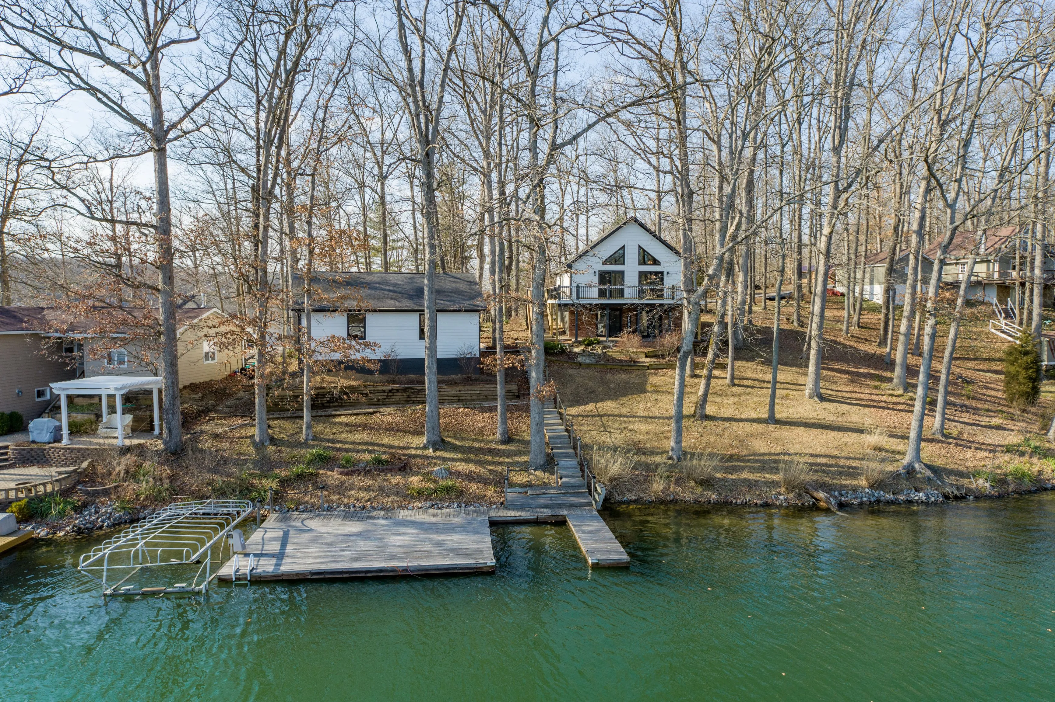 Lakeside house surrounded by leafless trees with a dock and boat slip in the foreground.