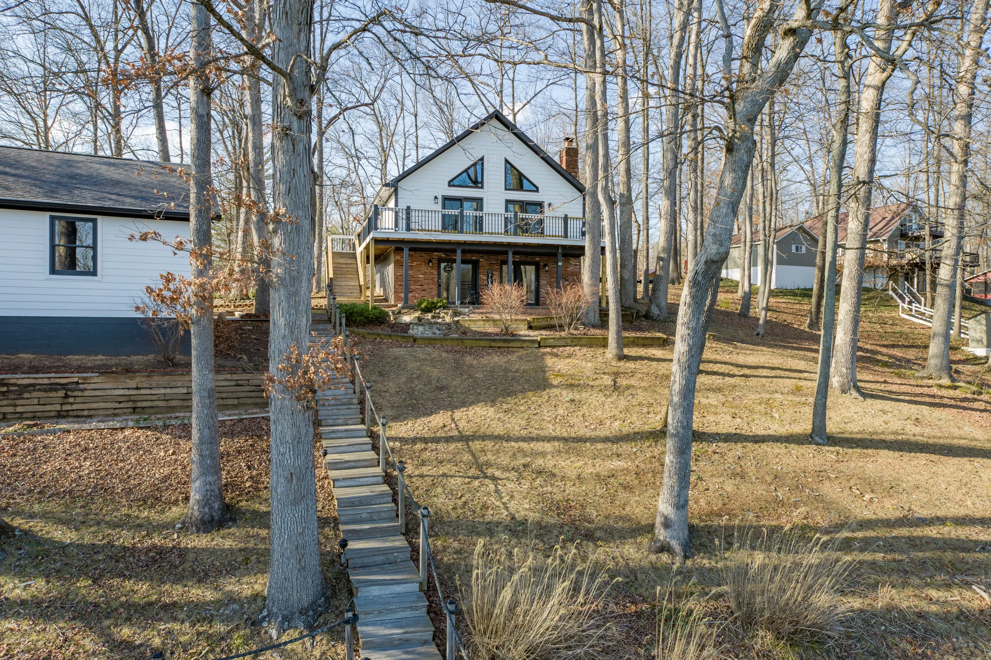 A cozy two-story house with a front porch, surrounded by bare trees and a lawn covered with brown leaves, a stone walkway leads up to the house.