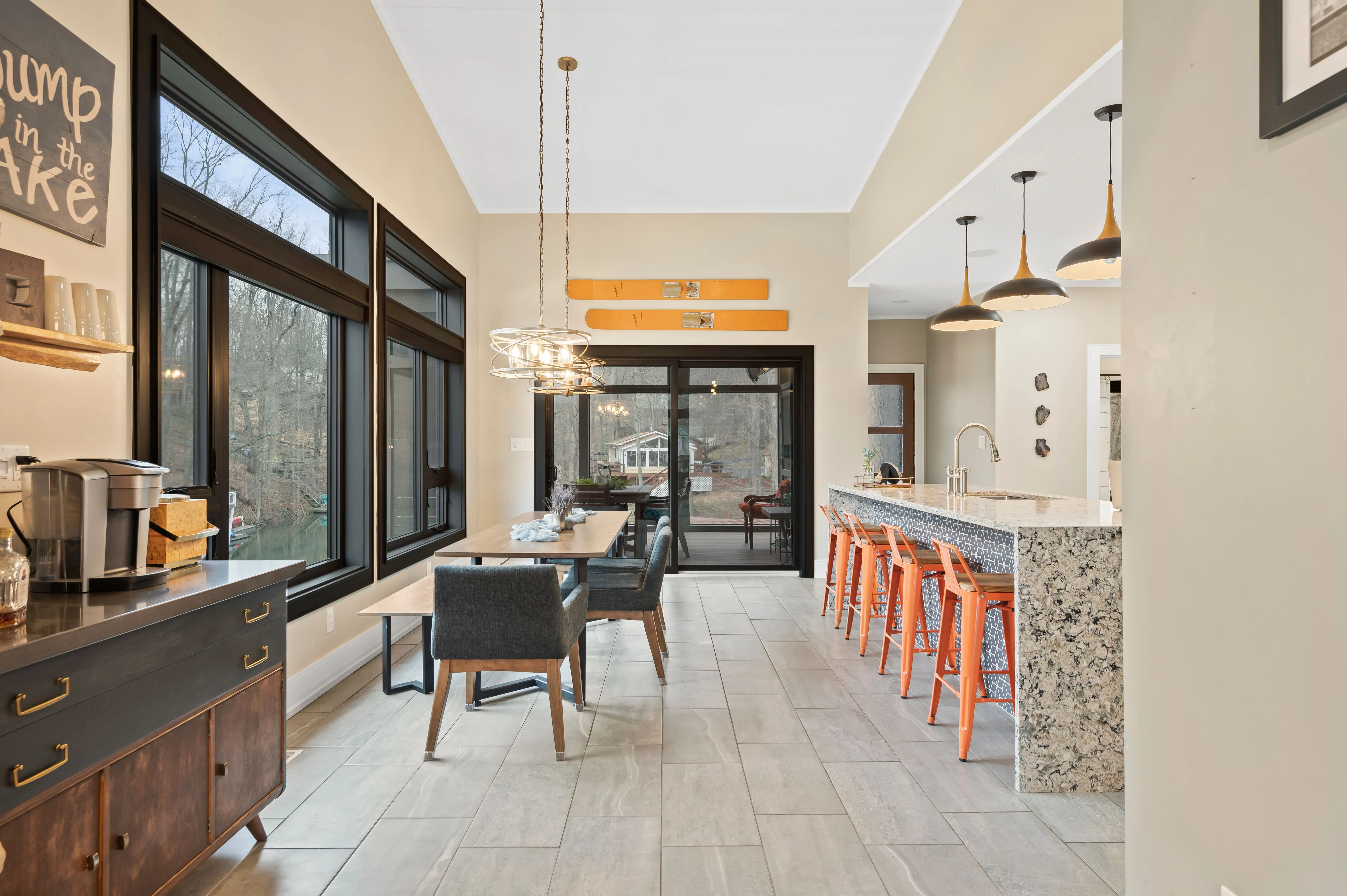 Modern kitchen with bar stools, pendant lights, and a dining area visible in the background.