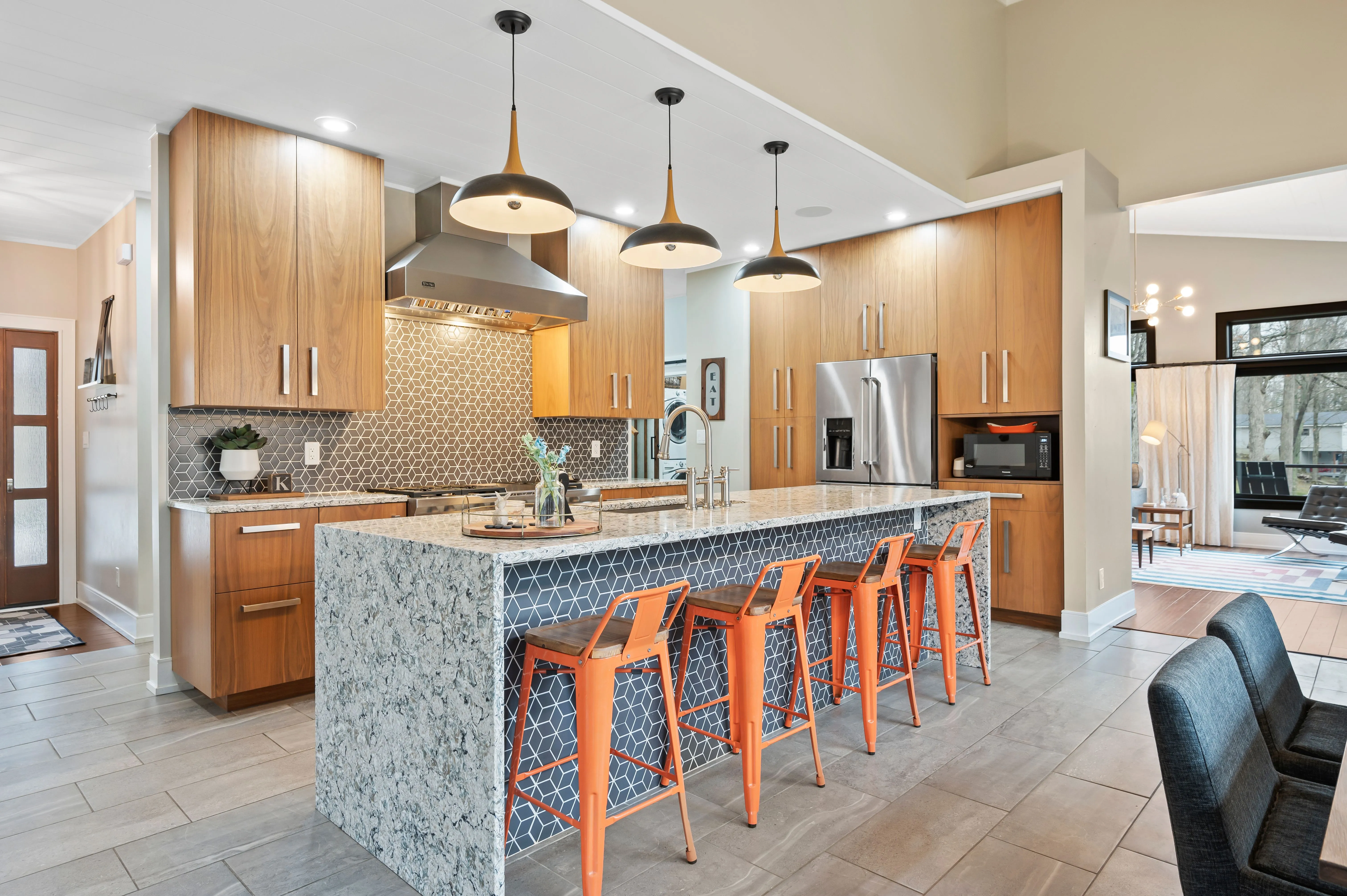 Modern kitchen interior with island and bar stools, wooden cabinetry, and stainless steel appliances.