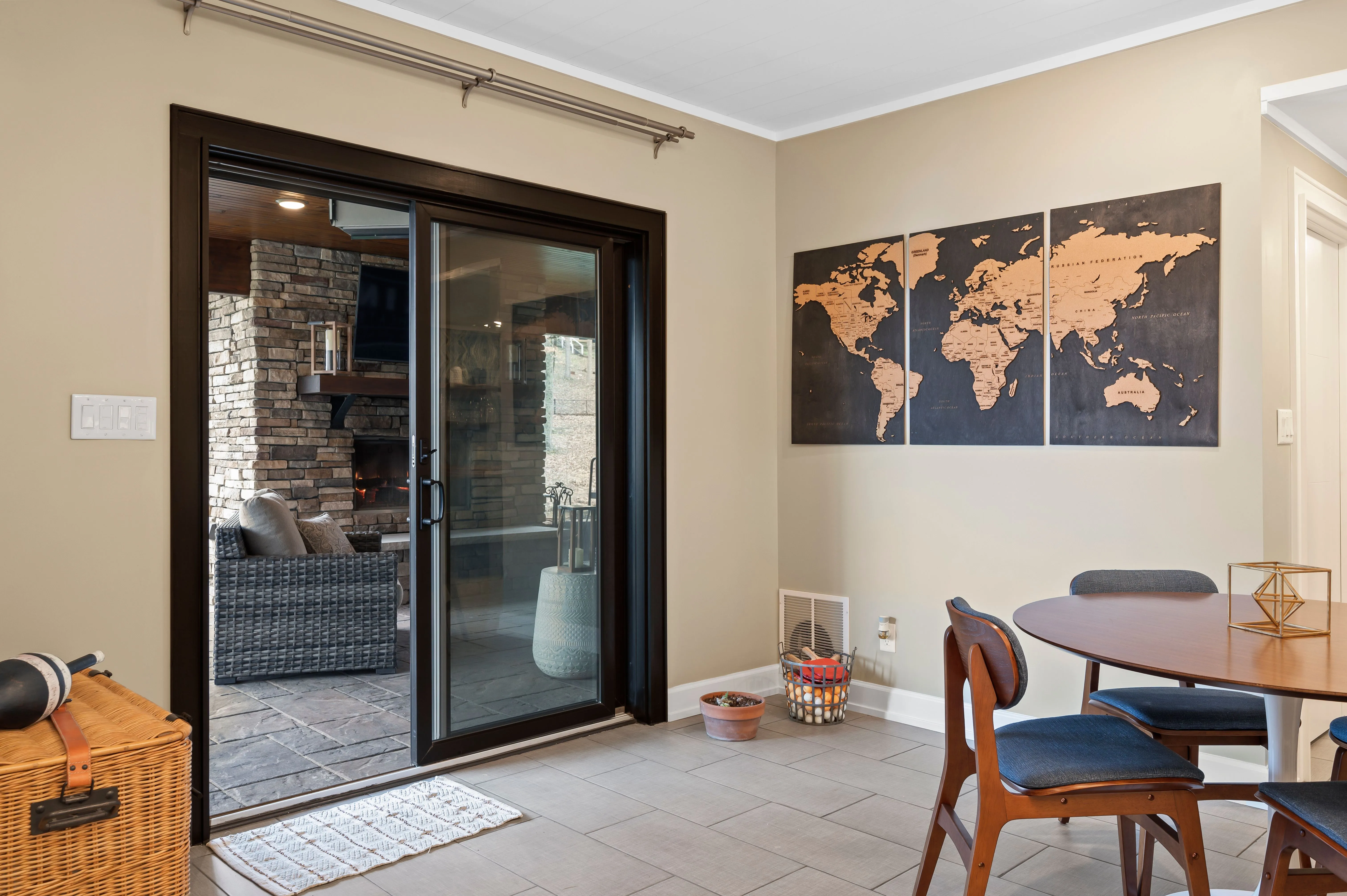 Interior view of a modern room with sliding glass door, world map wall art, wooden dining table with chairs, and a wicker basket.