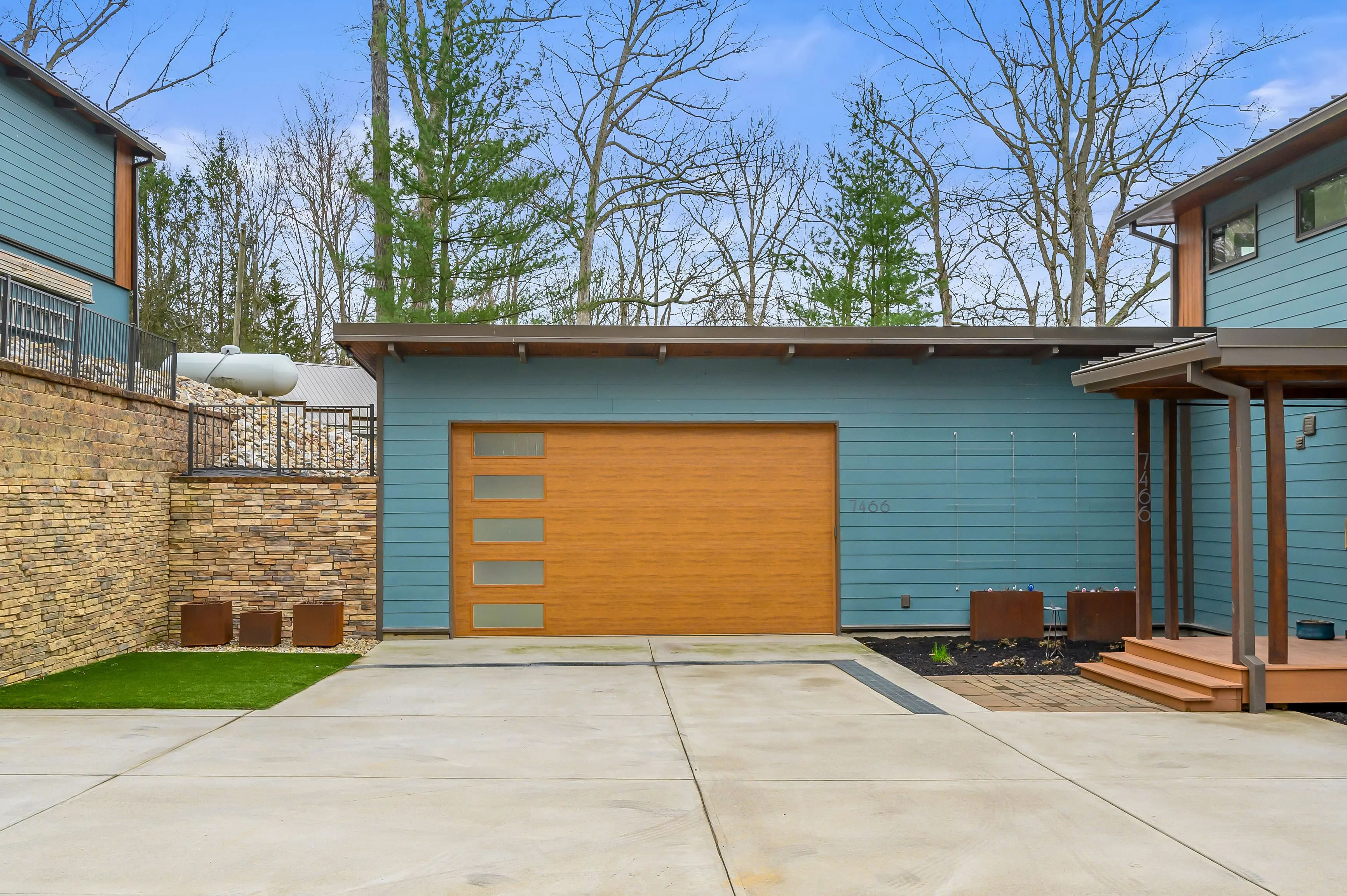 Exterior view of a modern home with a blue facade and wooden garage door, concrete driveway, and a landscaped yard.