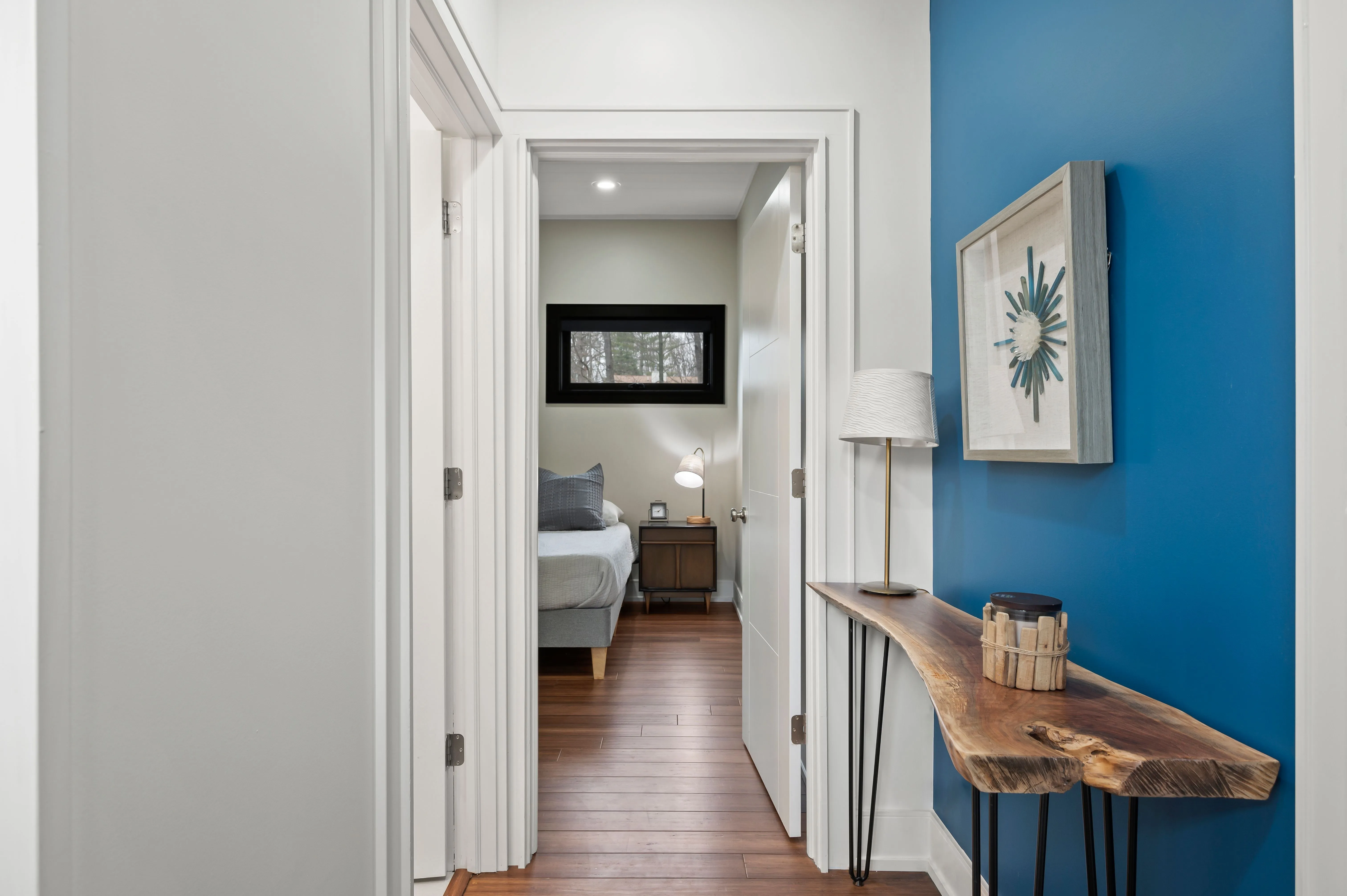 Bright hallway with contrasting blue and white walls, hardwood floors, and decorative table with plants.