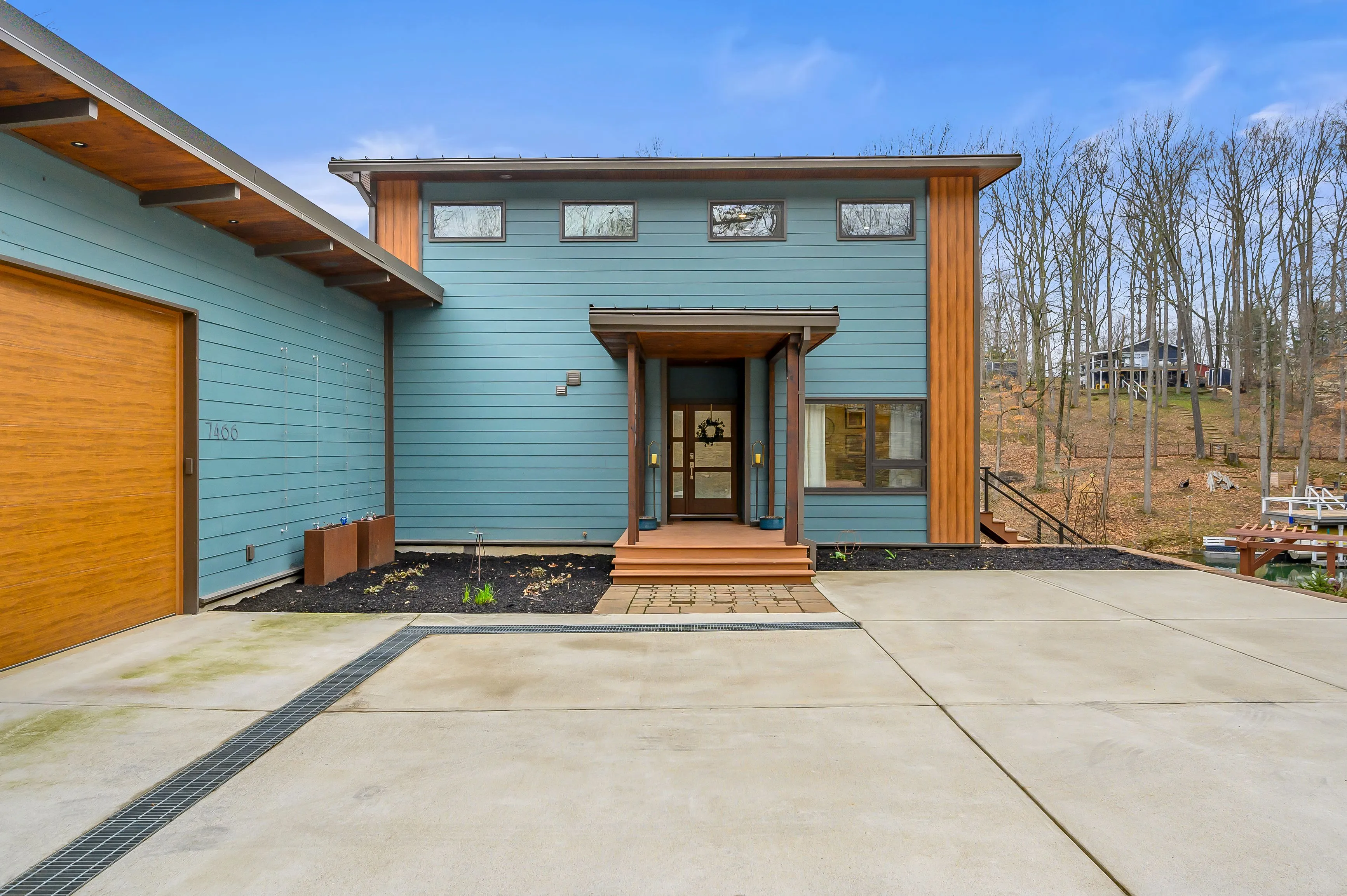 Modern two-story house with blue siding, wooden accents, and a concrete driveway.