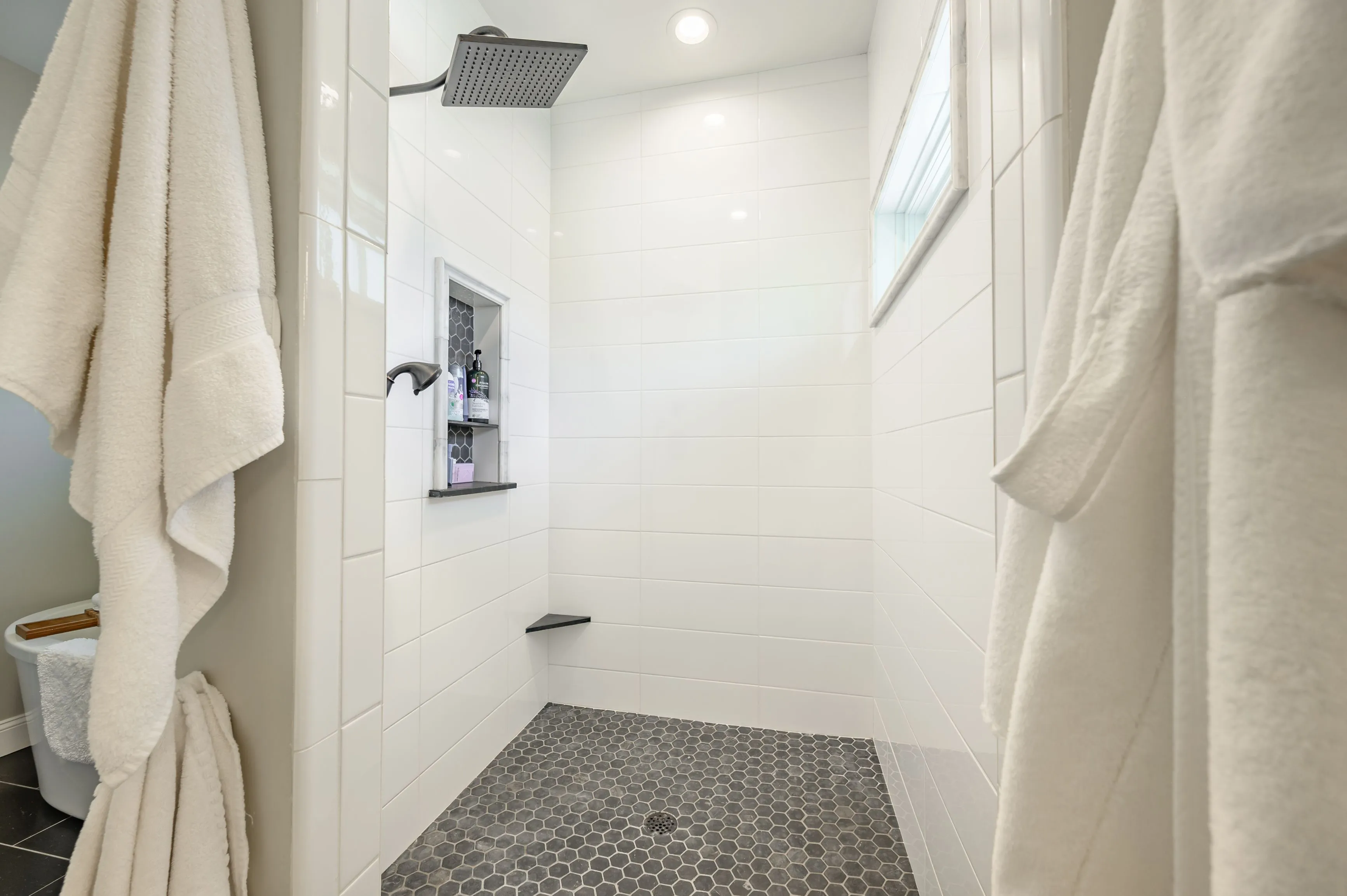 Modern bathroom with white curtains, a walk-in shower with dark tile flooring, and a wall-mounted shower head.