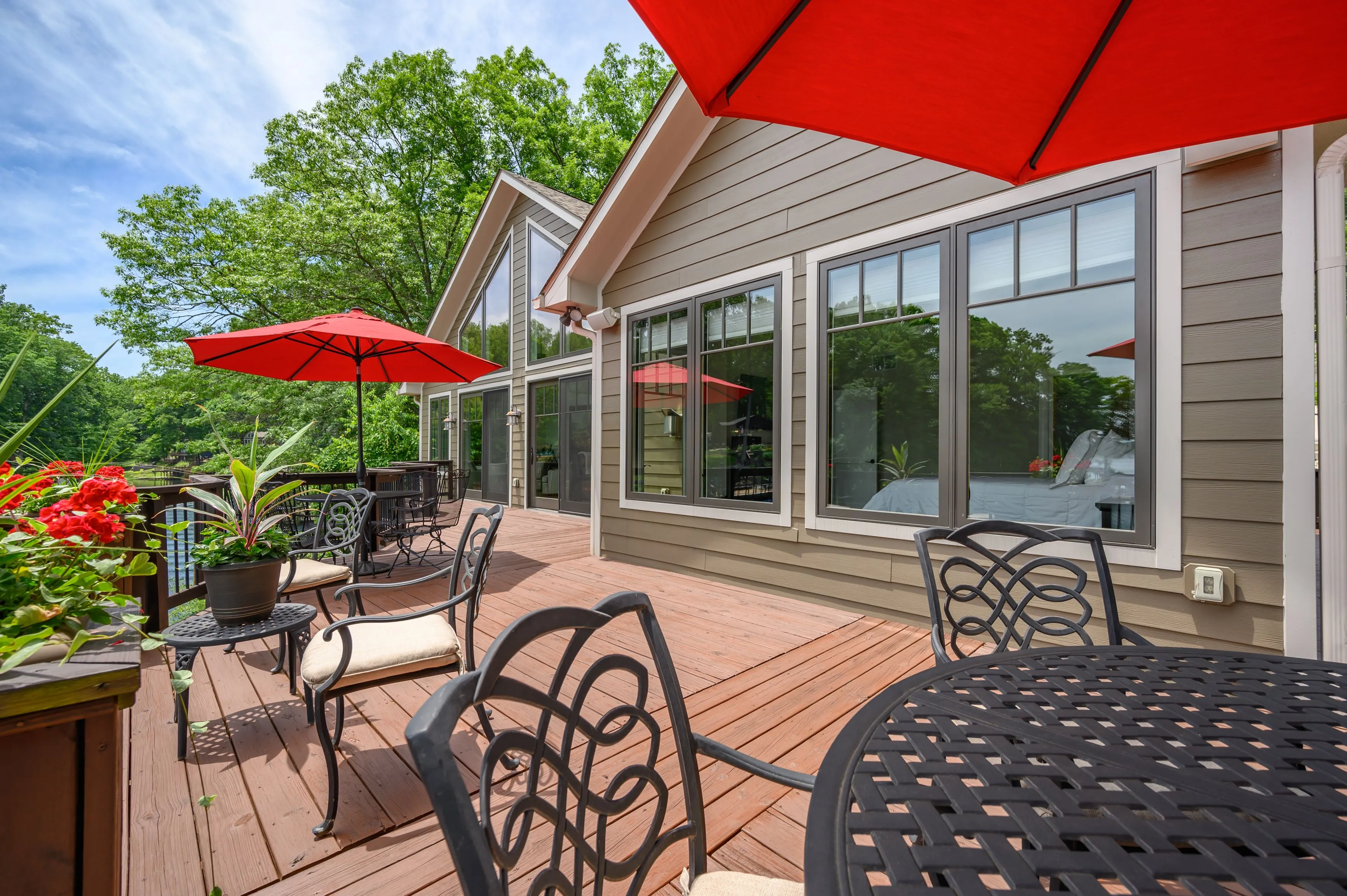 Wooden deck of a house with outdoor furniture and a red umbrella on a sunny day.