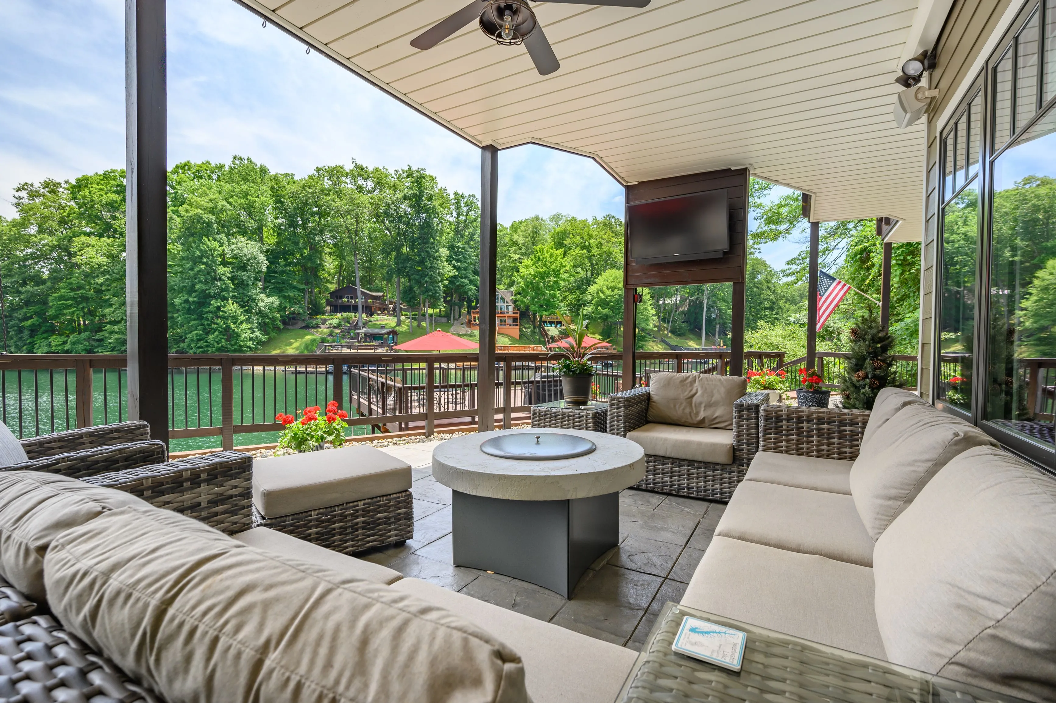 Covered patio area with comfortable outdoor seating, a fire pit, and a lush green forest view in the background.