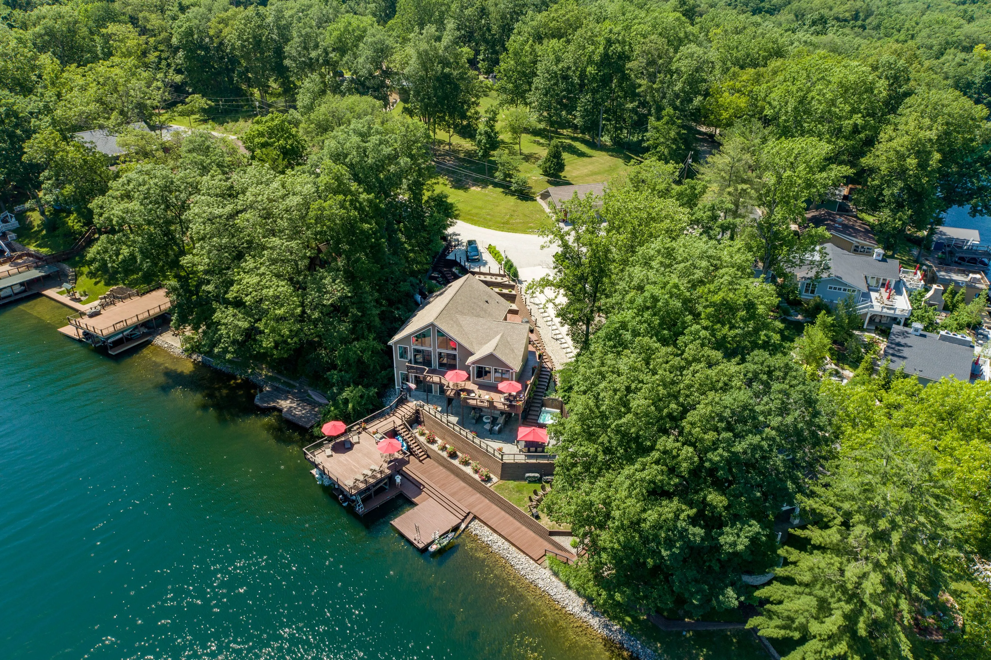 Aerial view of a lakeside house surrounded by lush greenery with a dock and boats.