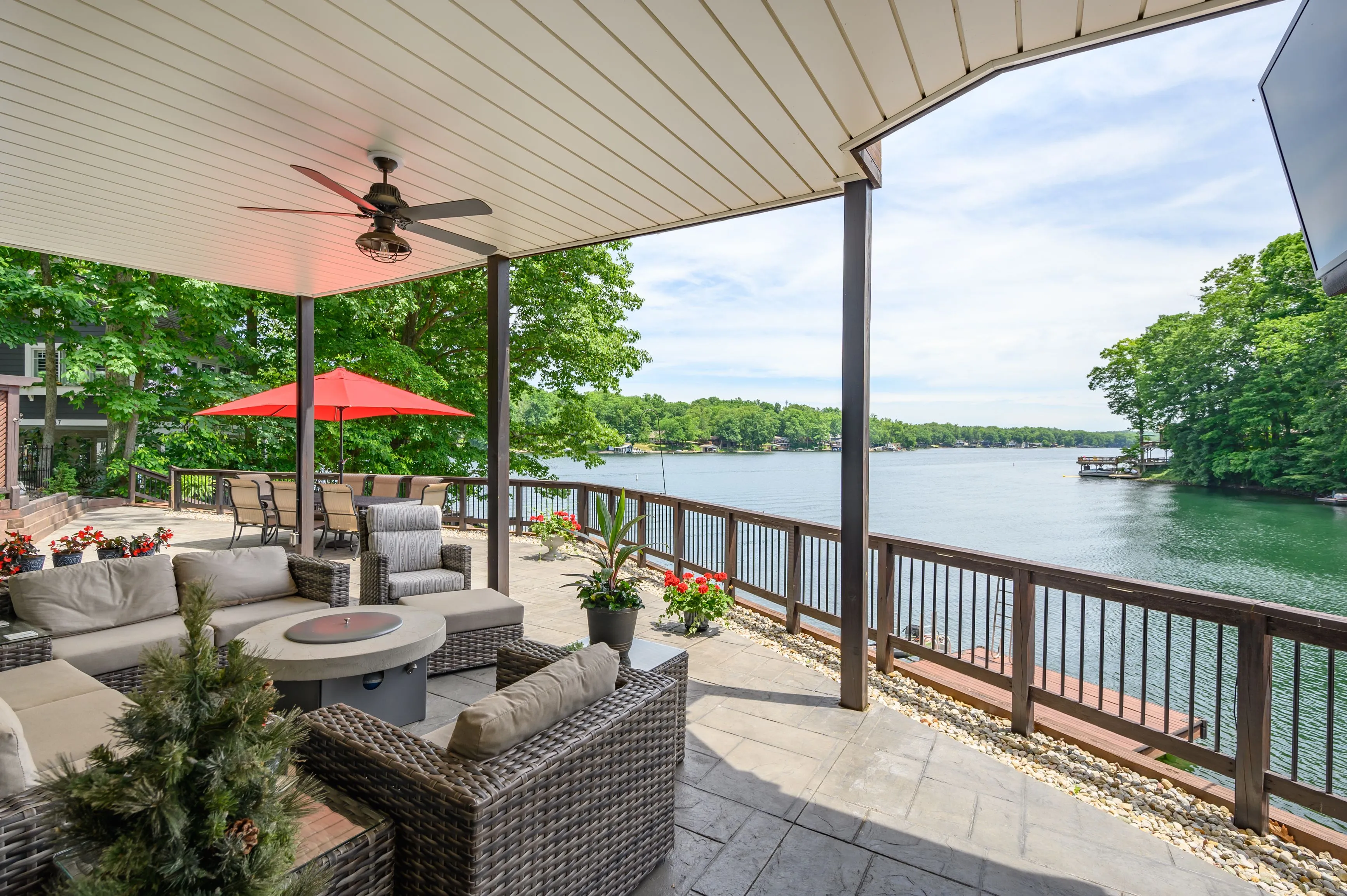 Outdoor patio with comfortable seating overlooking a calm lake with greenery in the background.