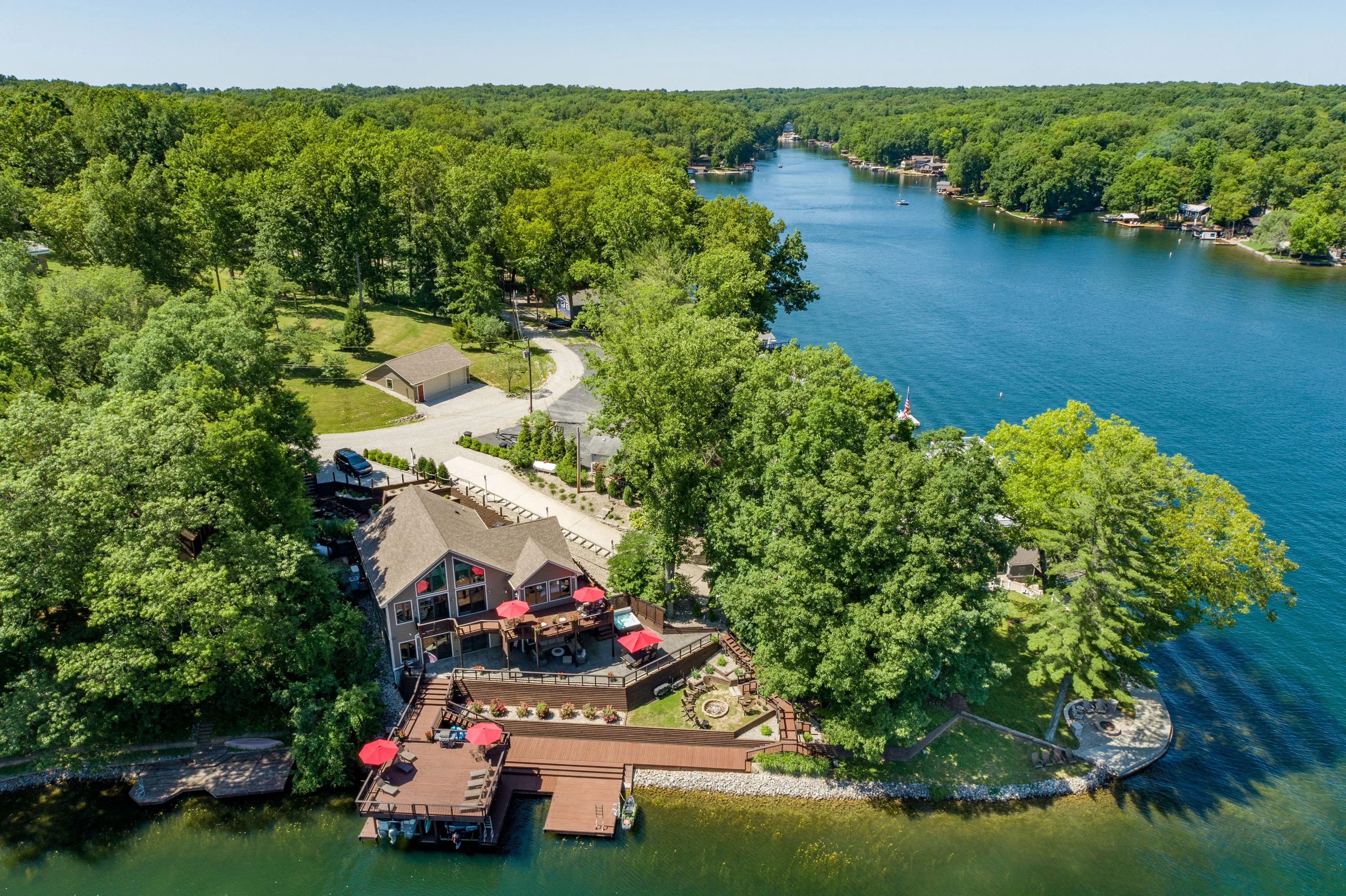 Aerial view of lakeside houses surrounded by lush greenery with a clear blue sky above.