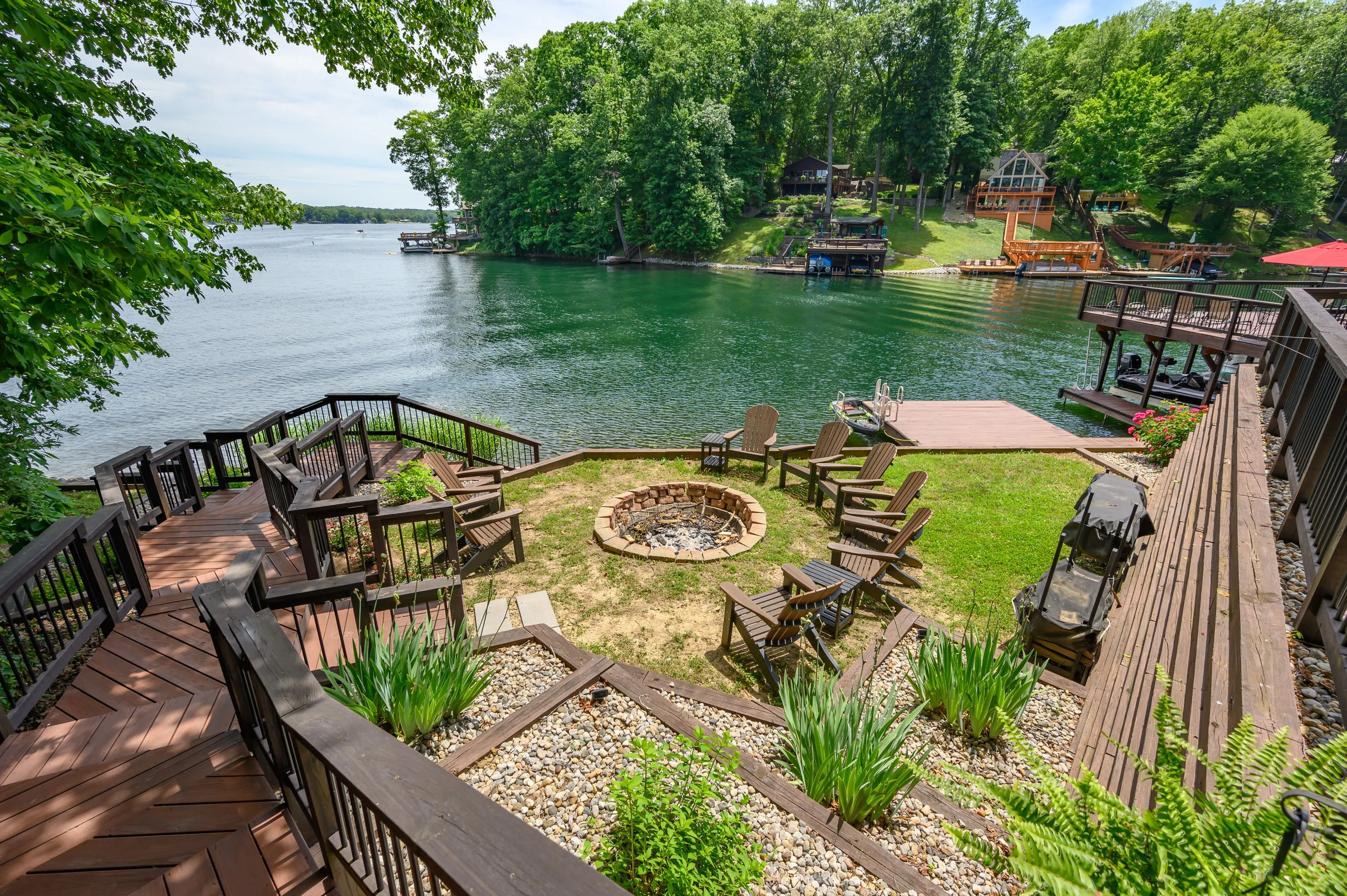 Lakeside backyard with a fire pit, seating area, and wooden stairs leading down to a dock.