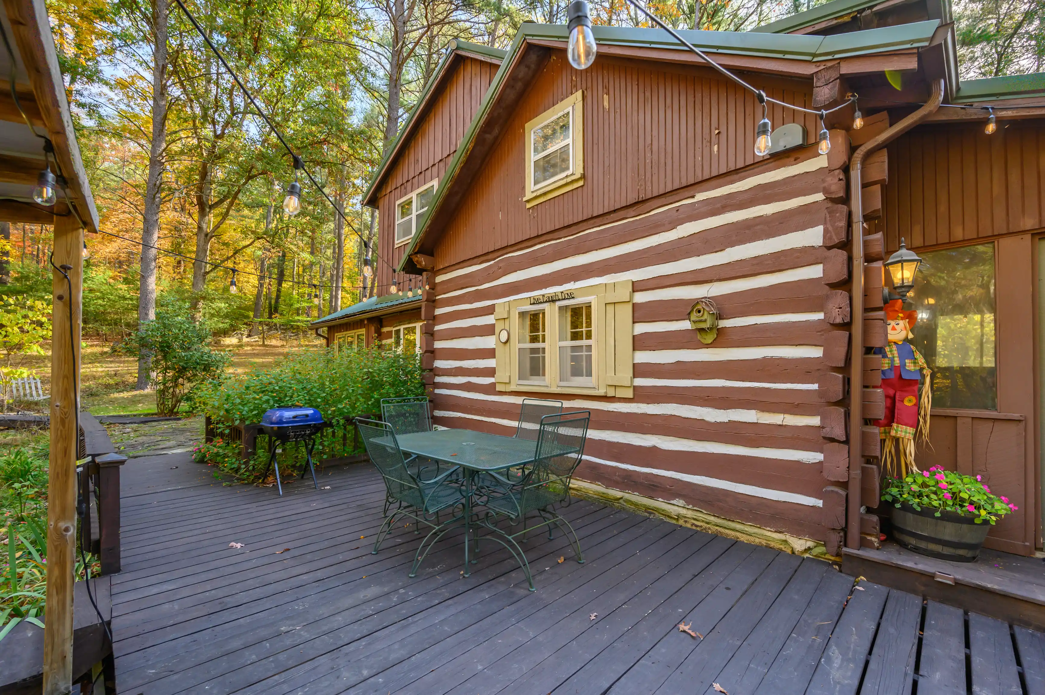 Cozy wooden cabin exterior with a deck area featuring a patio table and chairs surrounded by trees.