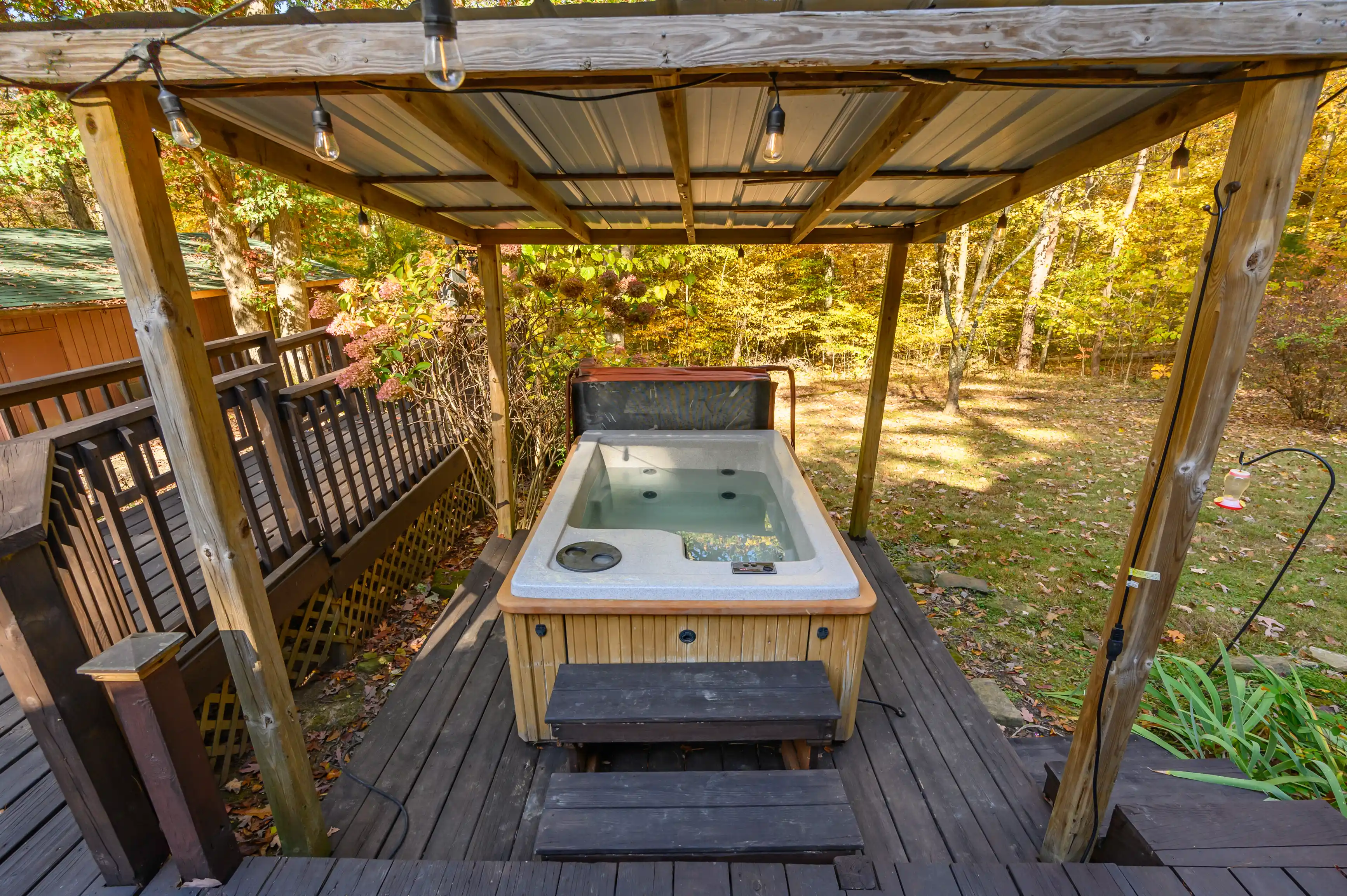 Outdoor jacuzzi under a wooden pergola on a deck surrounded by autumn foliage.