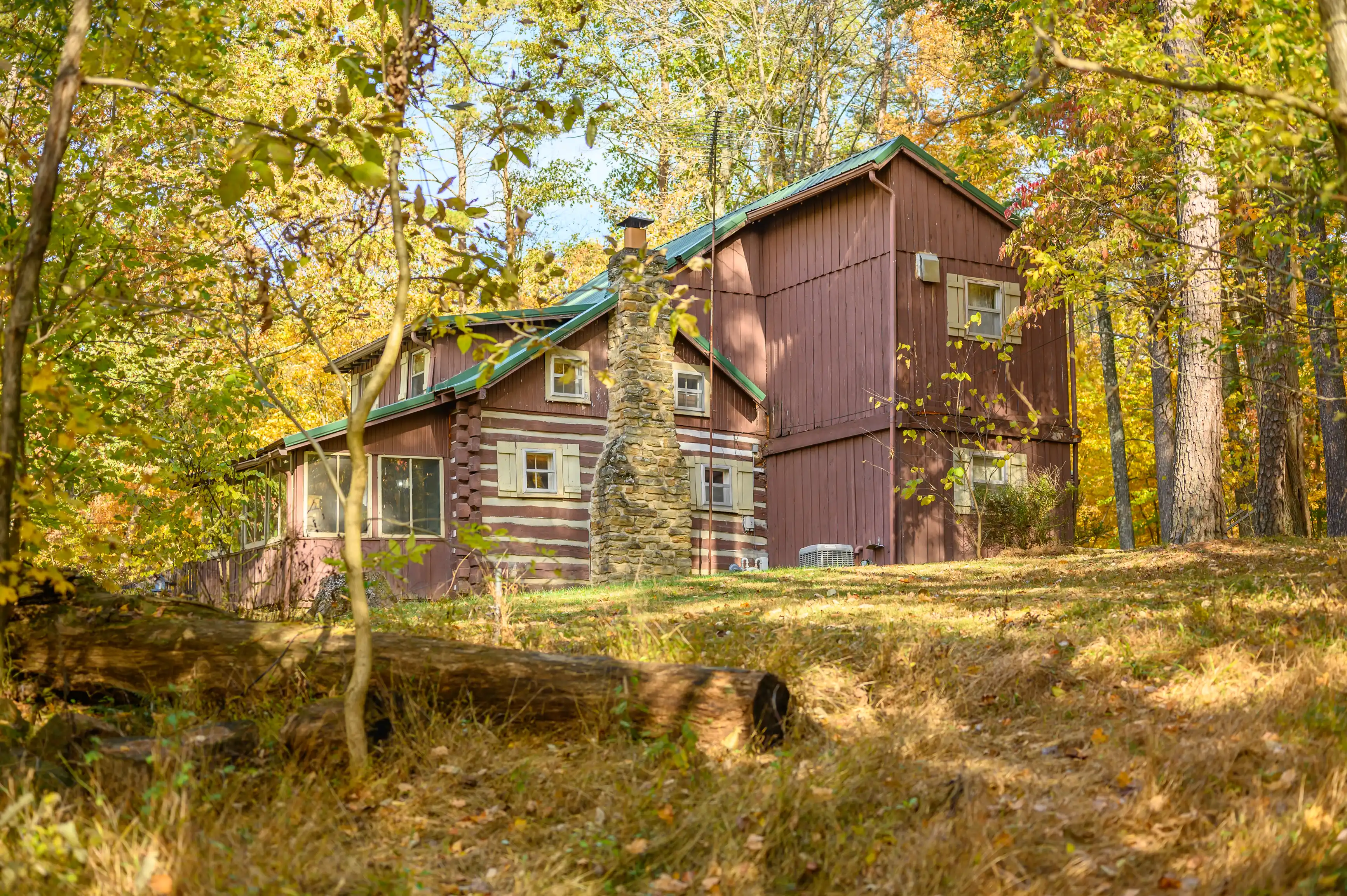 Rustic cabin surrounded by autumn trees with fallen leaves on the ground.