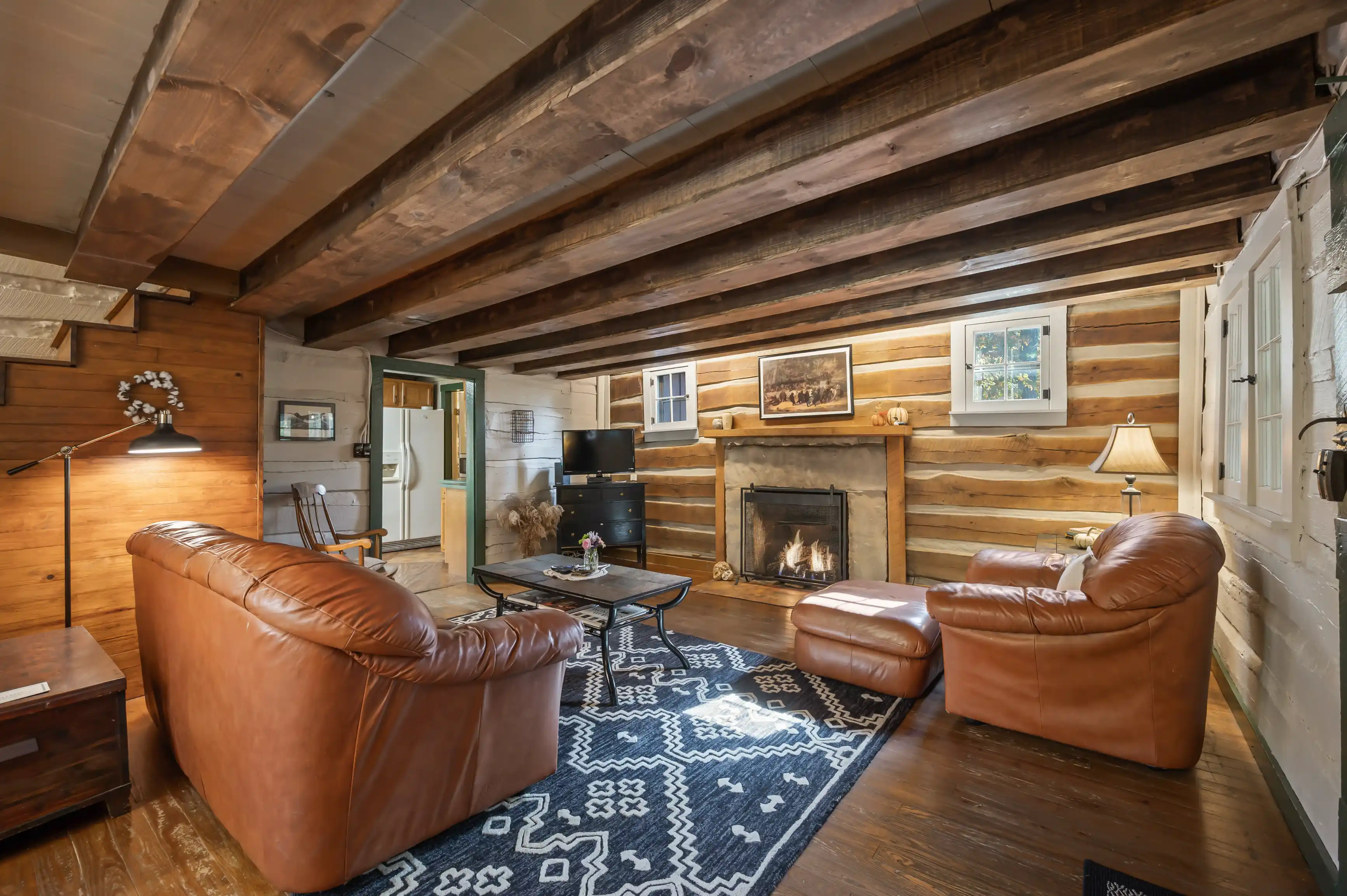 Cozy rustic living room interior with a fireplace, leather armchairs, and wooden beams on the ceiling.