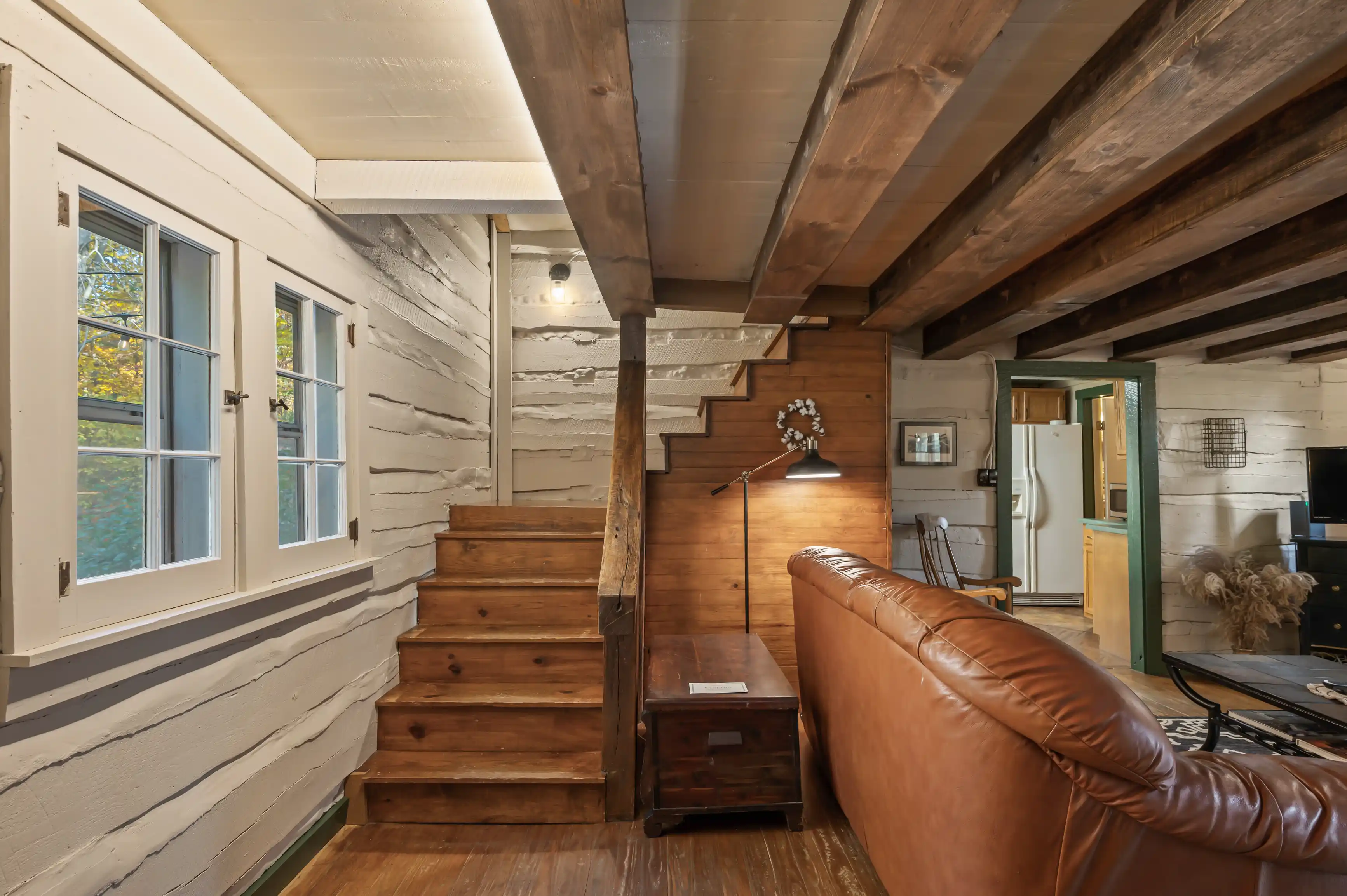 Interior of a cozy cabin with wooden stairs, walls, and beams, featuring a brown leather couch and modern amenities.
