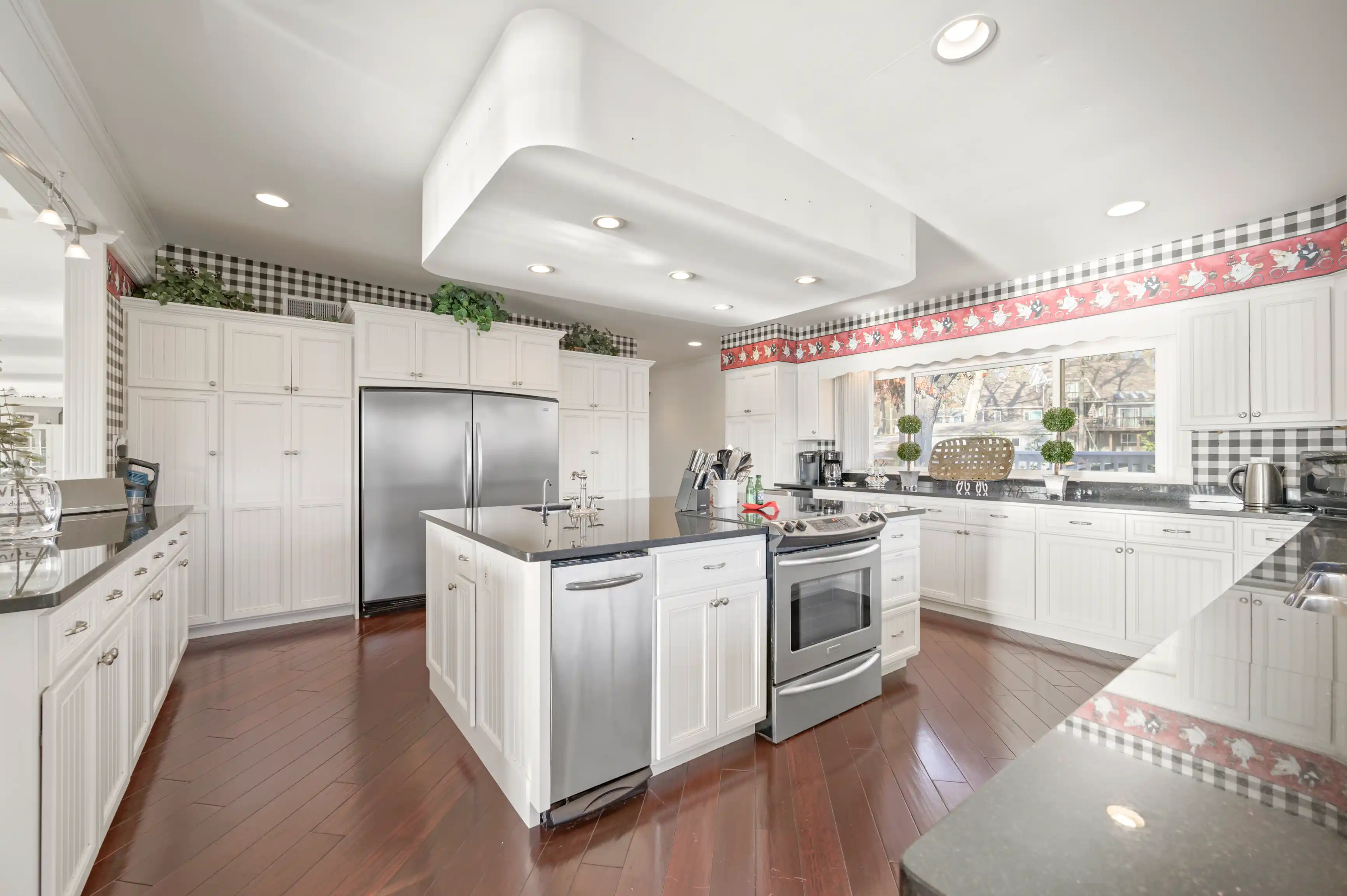 Spacious modern kitchen with white cabinetry, stainless steel appliances, and hardwood flooring.