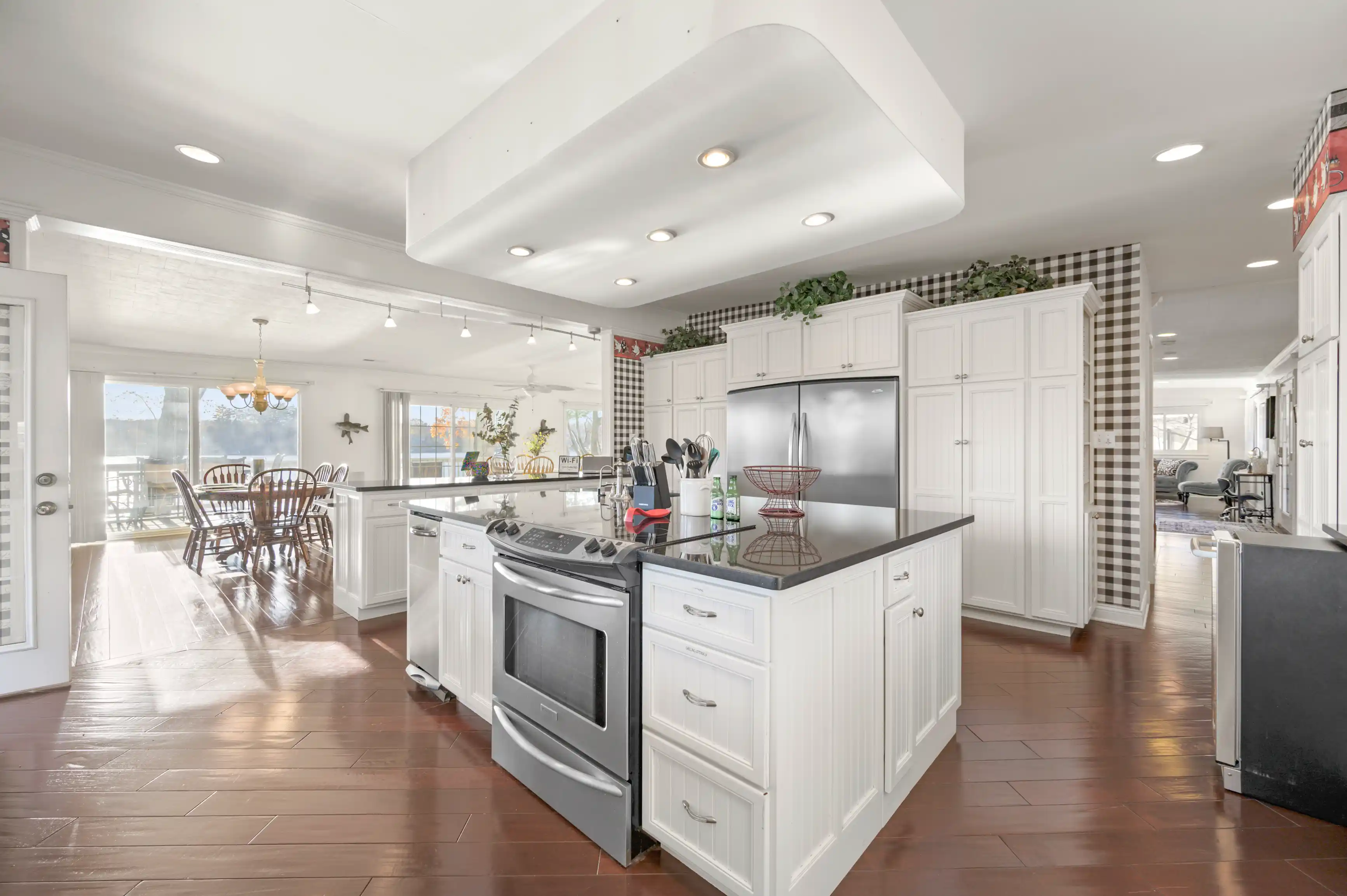 Bright and spacious kitchen with white cabinetry, stainless steel appliances, and a dining area with a wooden table set by large windows.