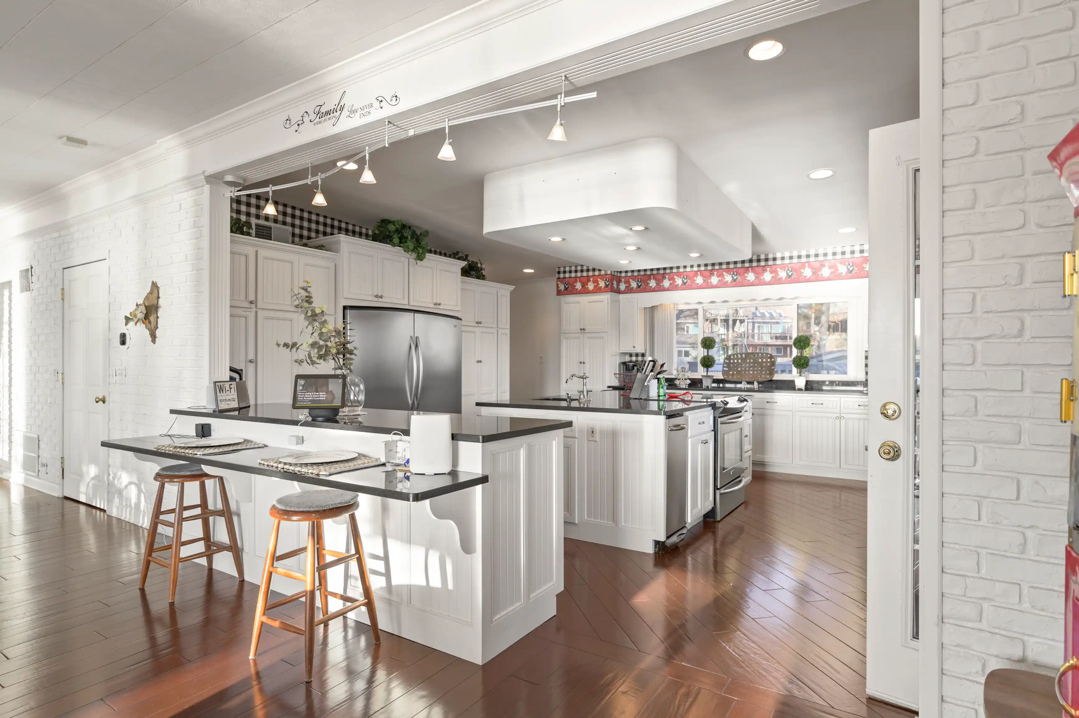 Bright and spacious kitchen interior with white cabinetry, stainless steel appliances, a central island with bar stools, and hardwood flooring.