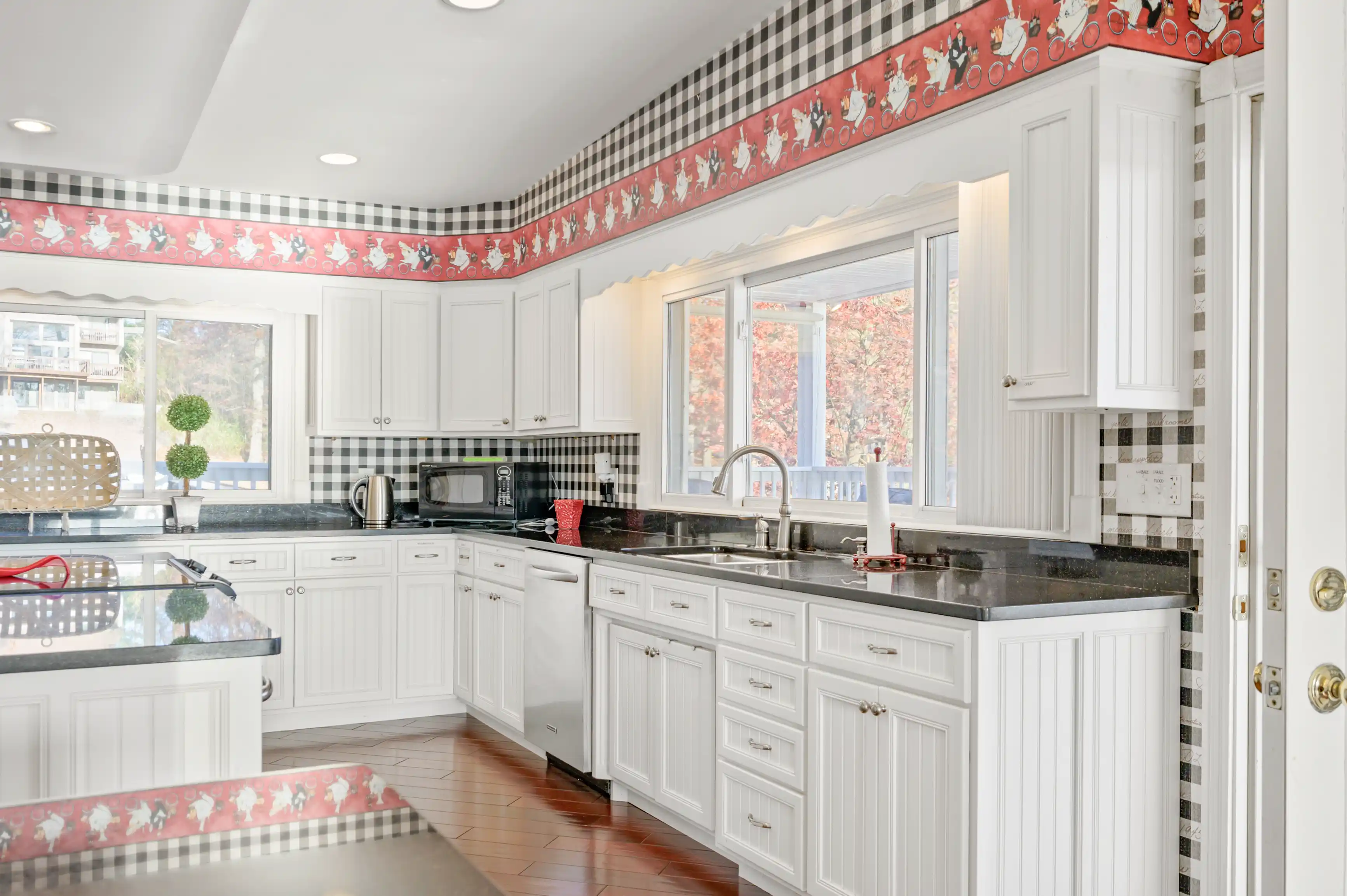 Bright kitchen interior with white cabinets, black countertops, and a checkered pattern with red accents on the border wallpaper.