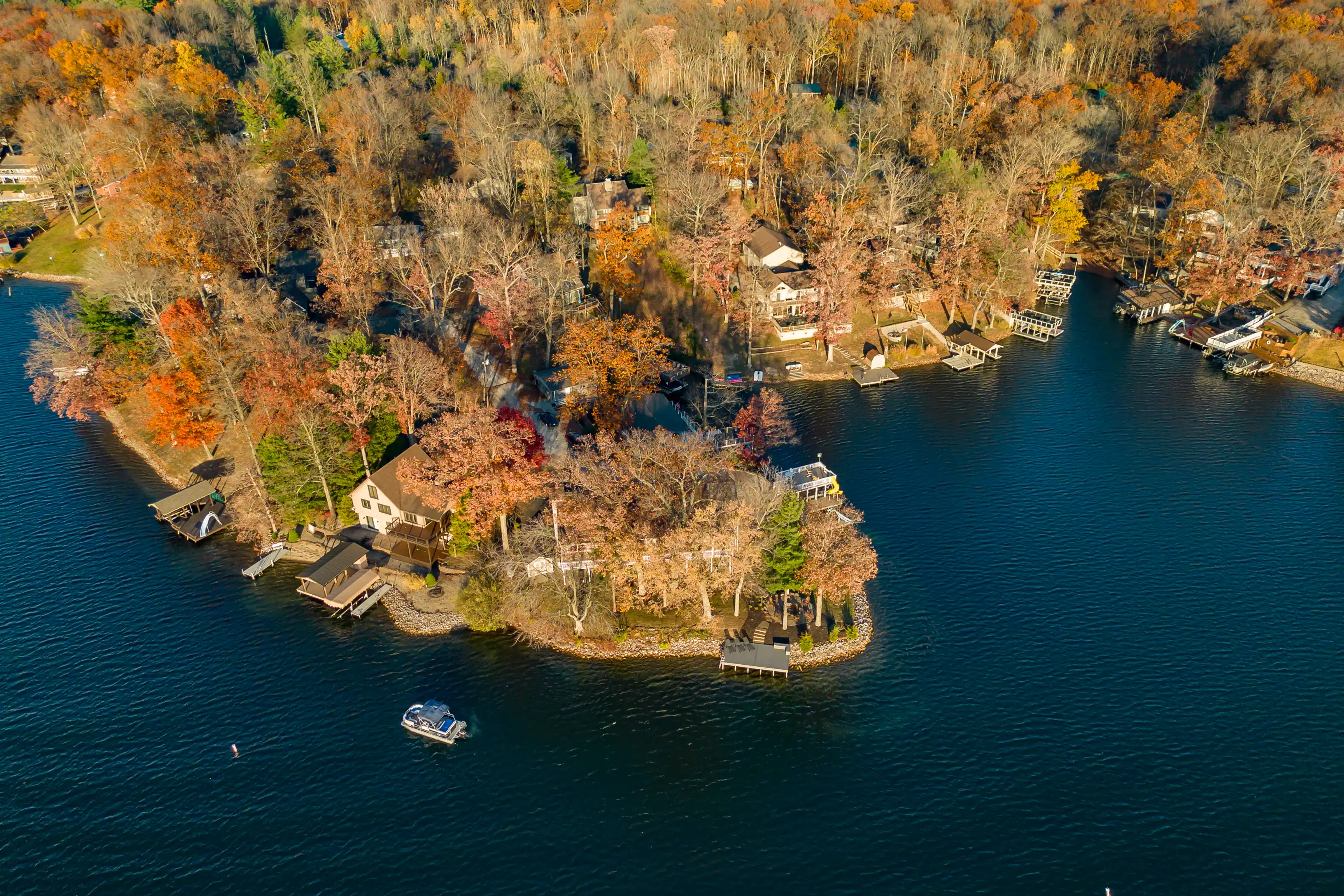 Aerial view of a peninsula with houses surrounded by a lake with docks and boats during autumn.