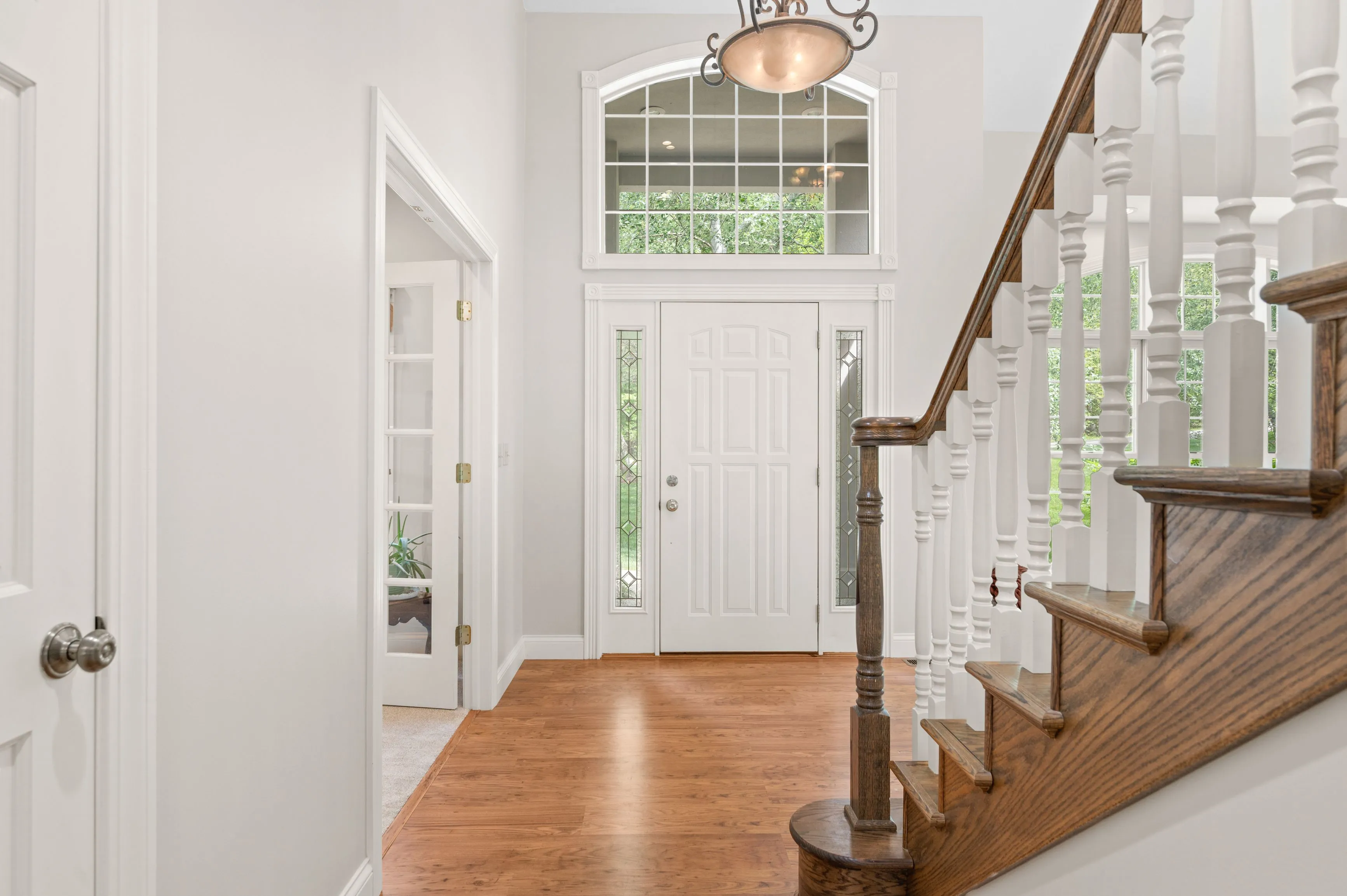 Bright and airy entryway with hardwood floors, a white front door with sidelights and transom window, and a wooden staircase with white spindles.