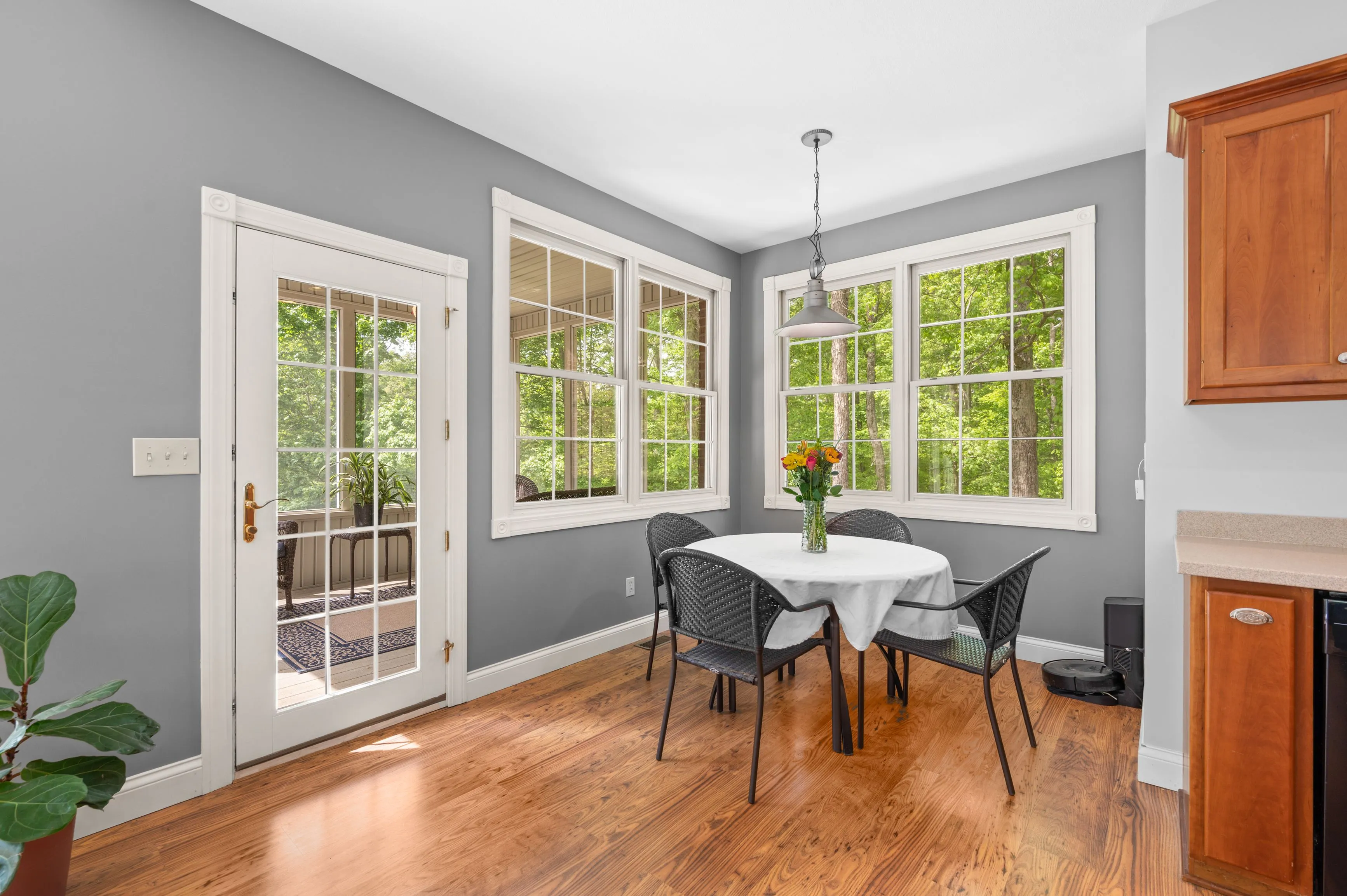 Bright dining area with hardwood floors, a round table with chairs, large windows with a view of trees, and French doors leading to a deck.